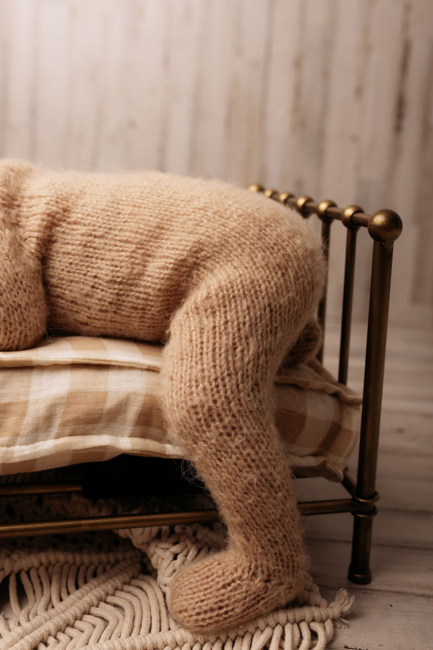 Cozy knit blanket draped over a vintage brass bed frame with plaid pillow on woven rug.