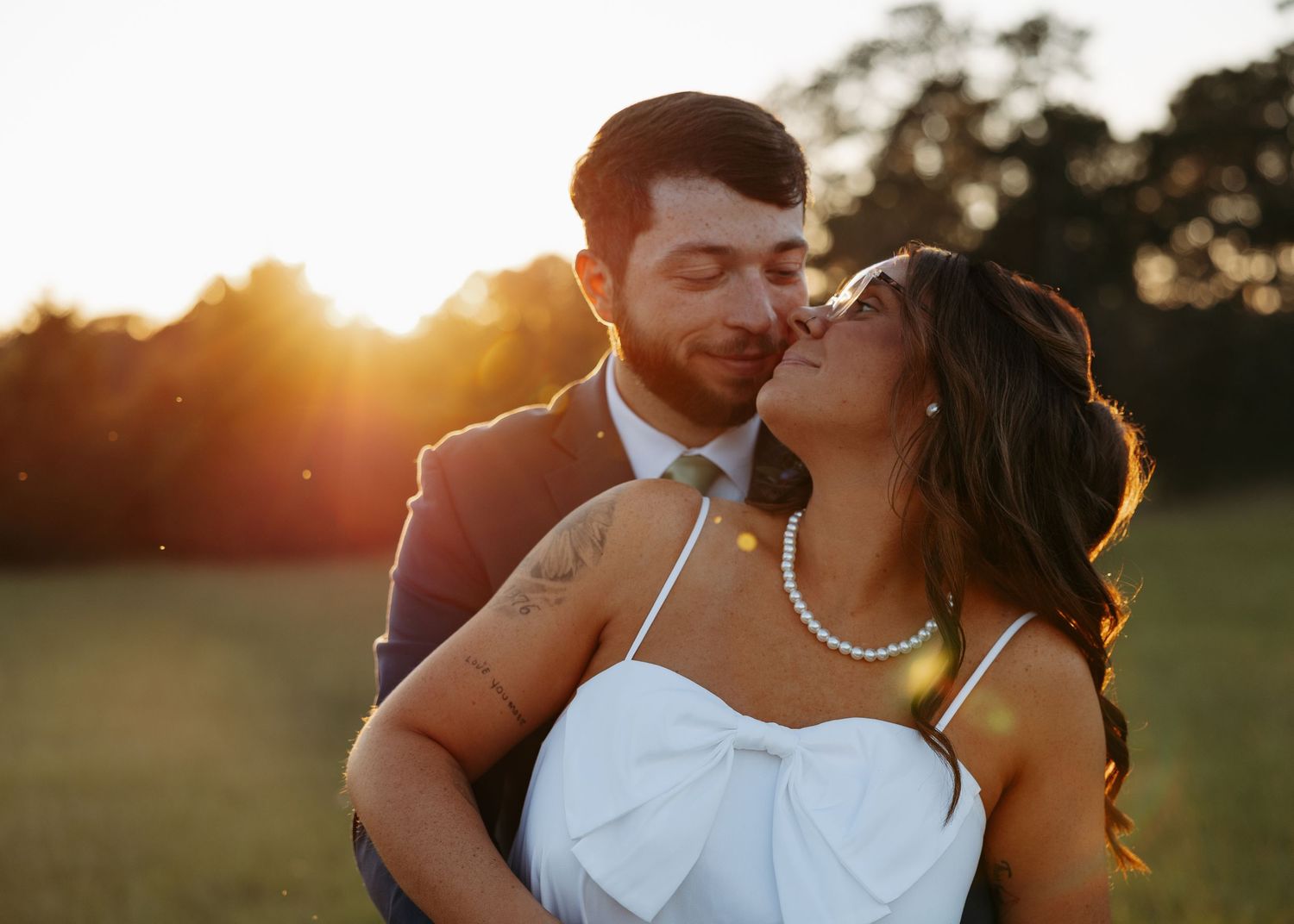 Bride and groom share a close romantic moment in golden sunset light outdoors.