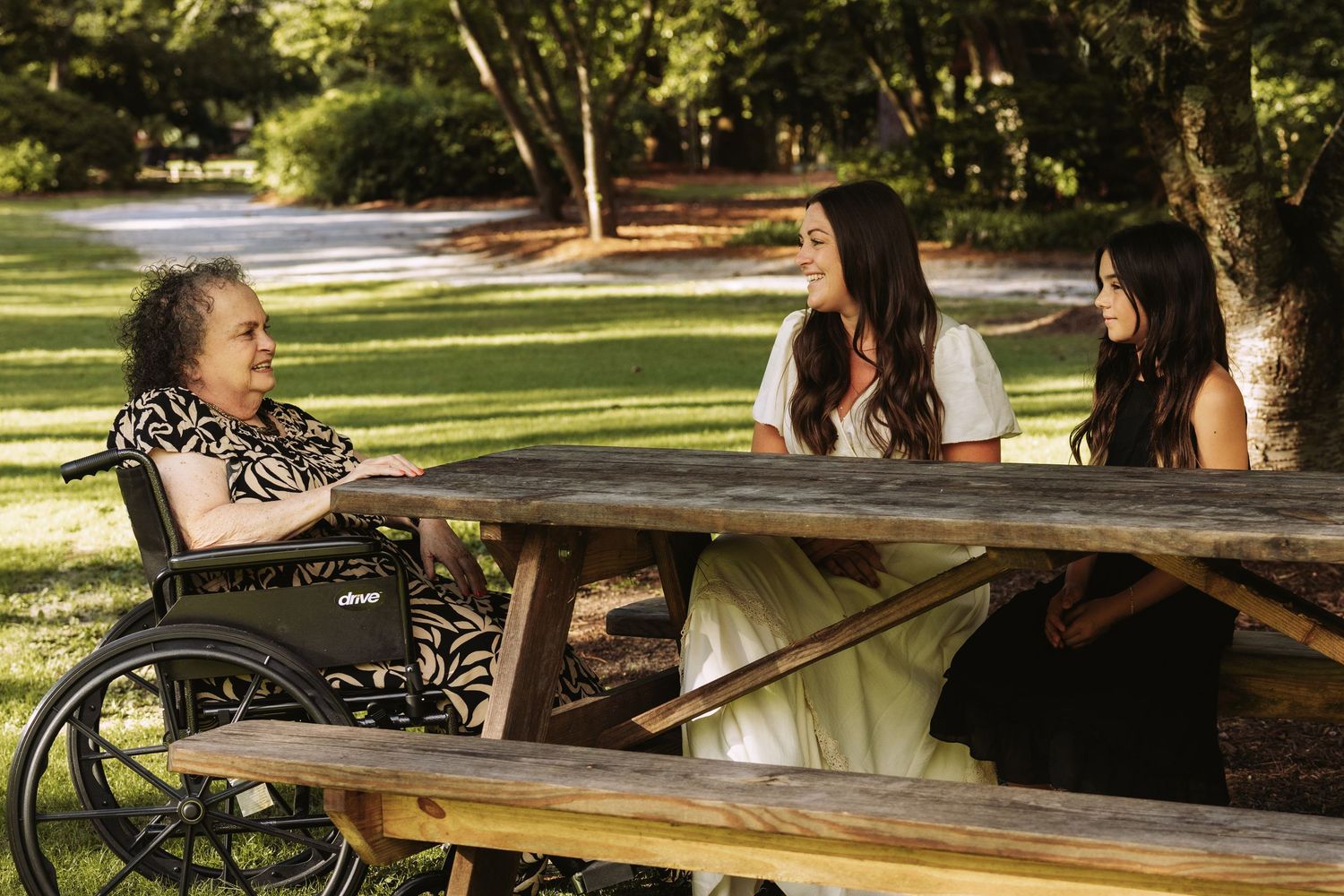 People sit at a wooden picnic table in a sunny park on a warm afternoon.