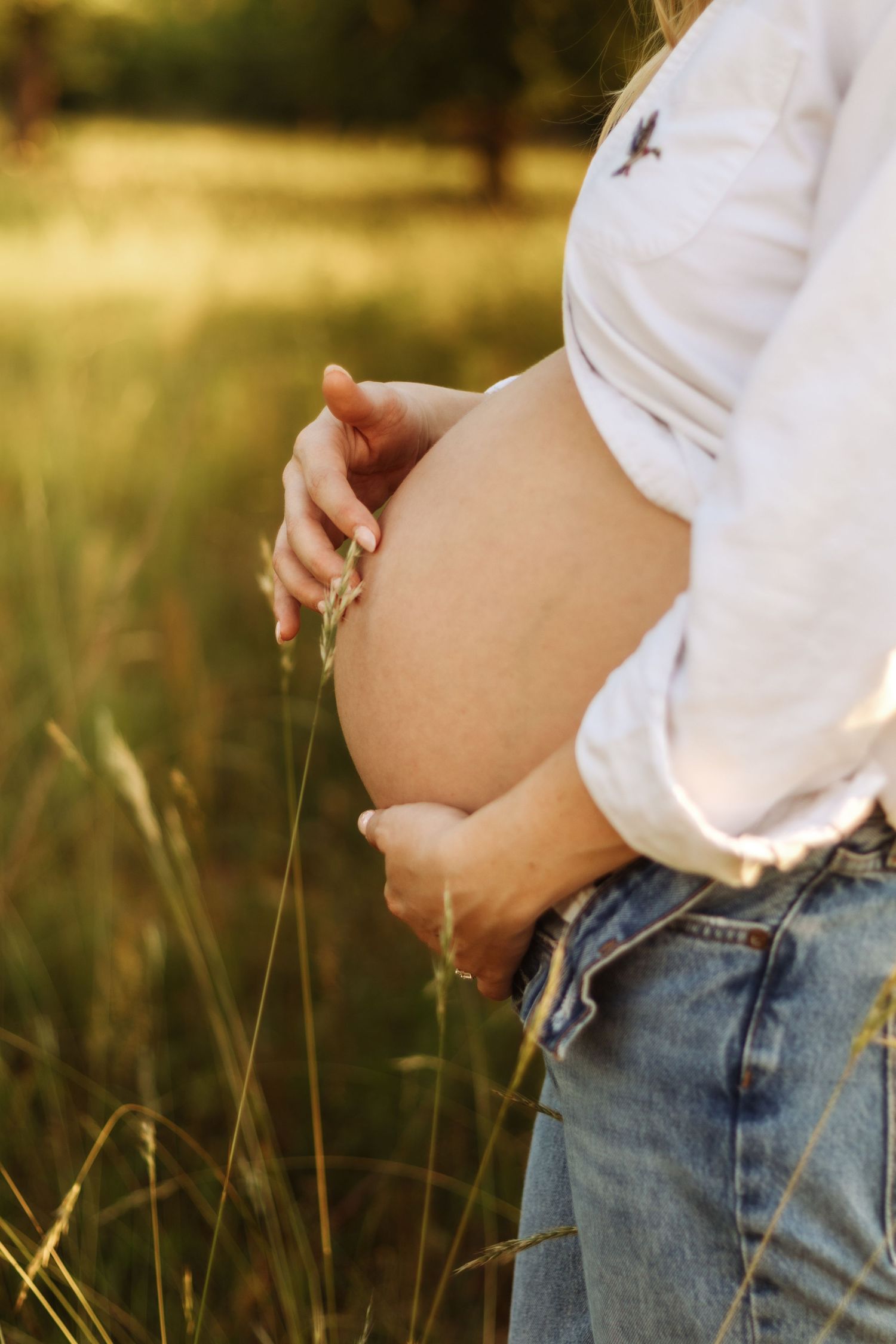Close-up shot of a pregnant belly with hands resting gently on it against a golden sunset backdrop.