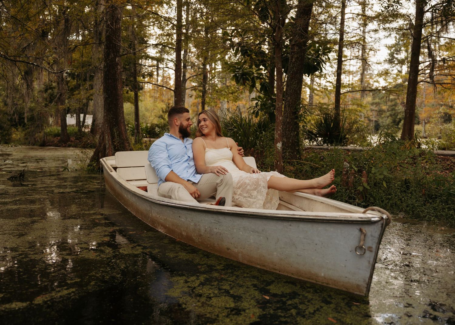 Couple relaxing together in a white canoe on a serene, tree-lined swamp during a romantic outdoor photo session.