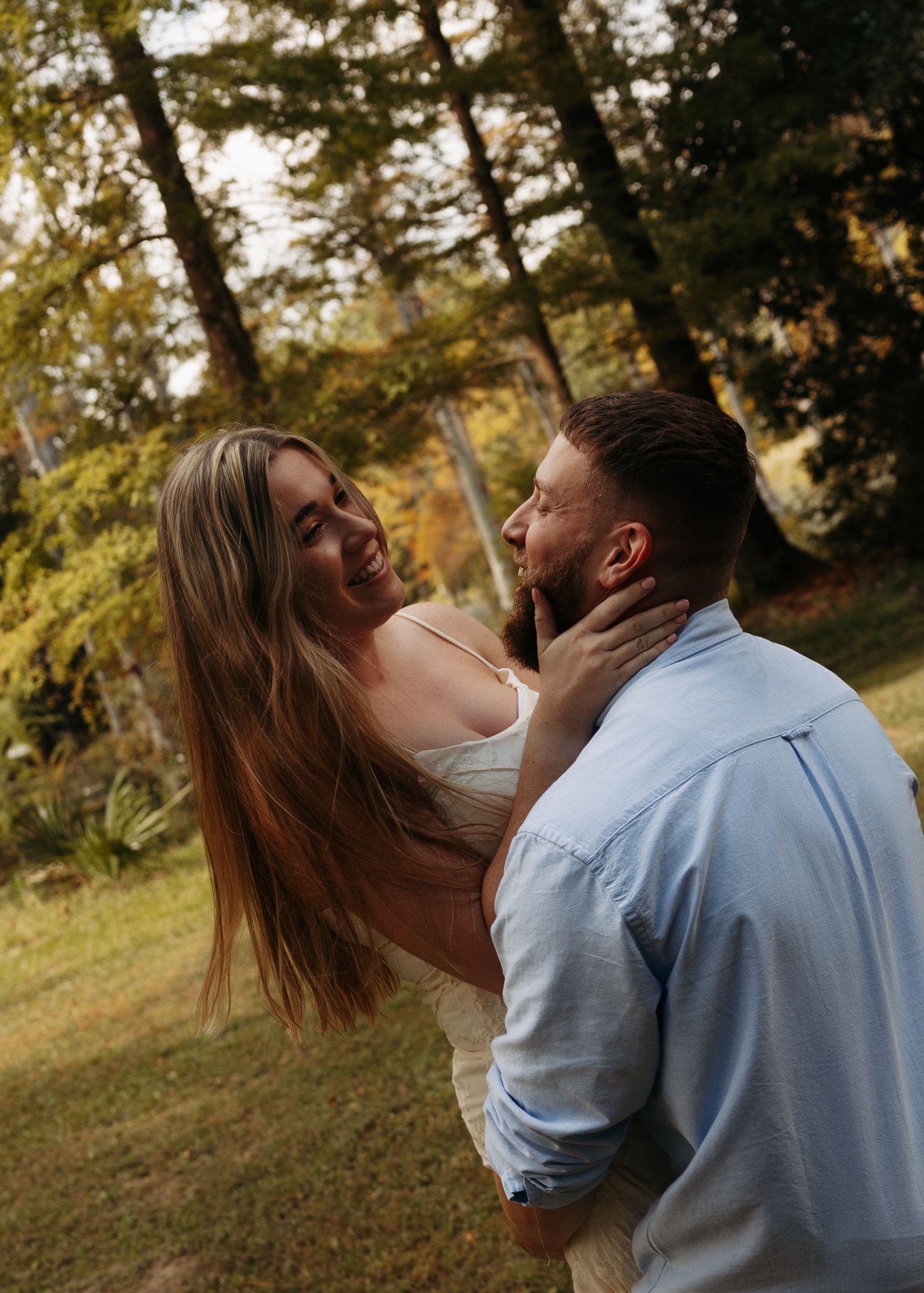 Couple embracing outdoors in a lush green park, woman tenderly holding mans face while gazing into each others eyes.