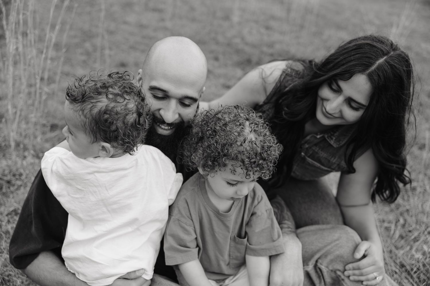 Black and white family photo of parents and two young children sitting together outdoors, smiling and embracing.