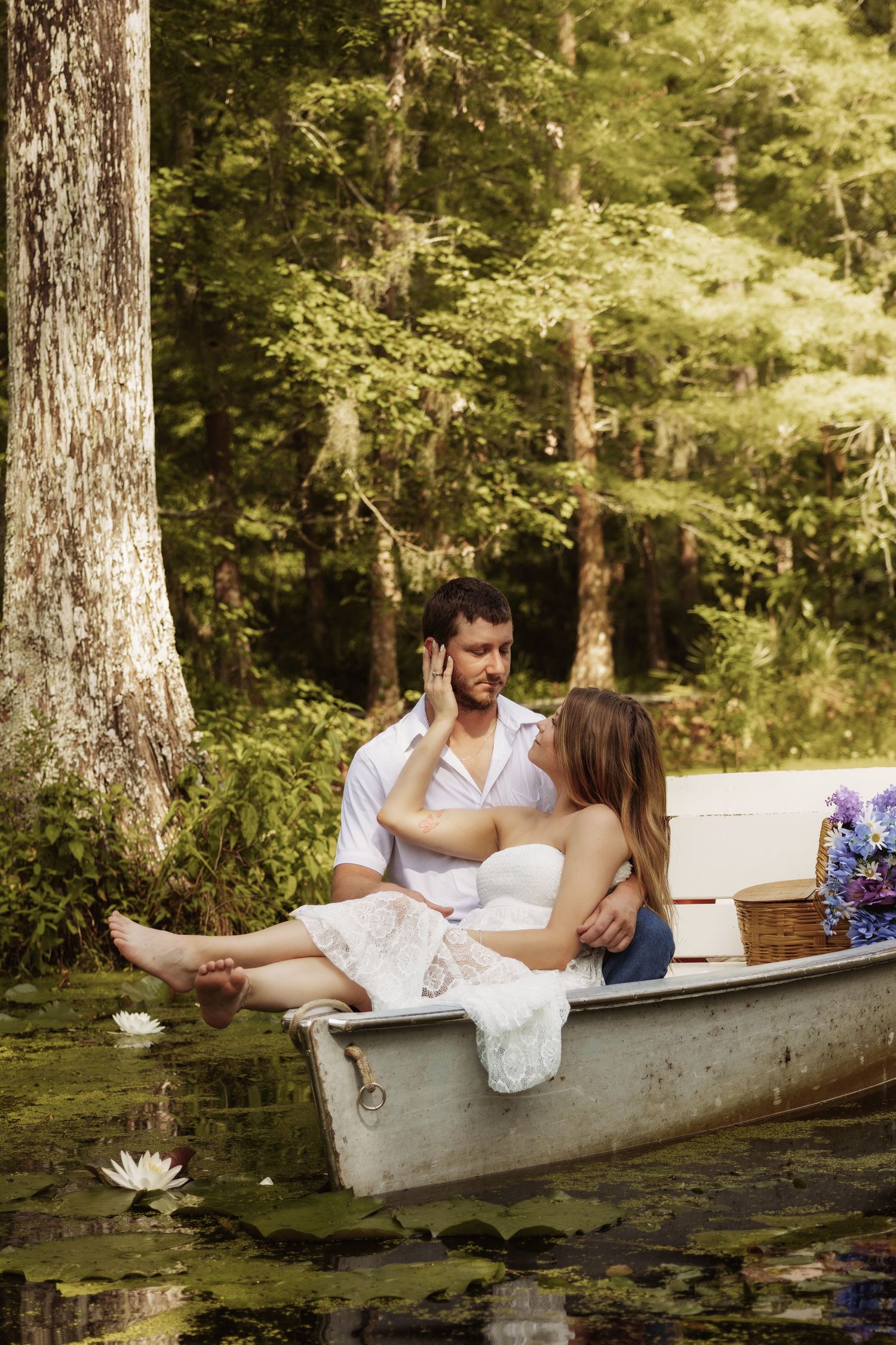 Romantic couple sitting together in a rowboat on a serene forest lake surrounded by lily pads and lush green trees.