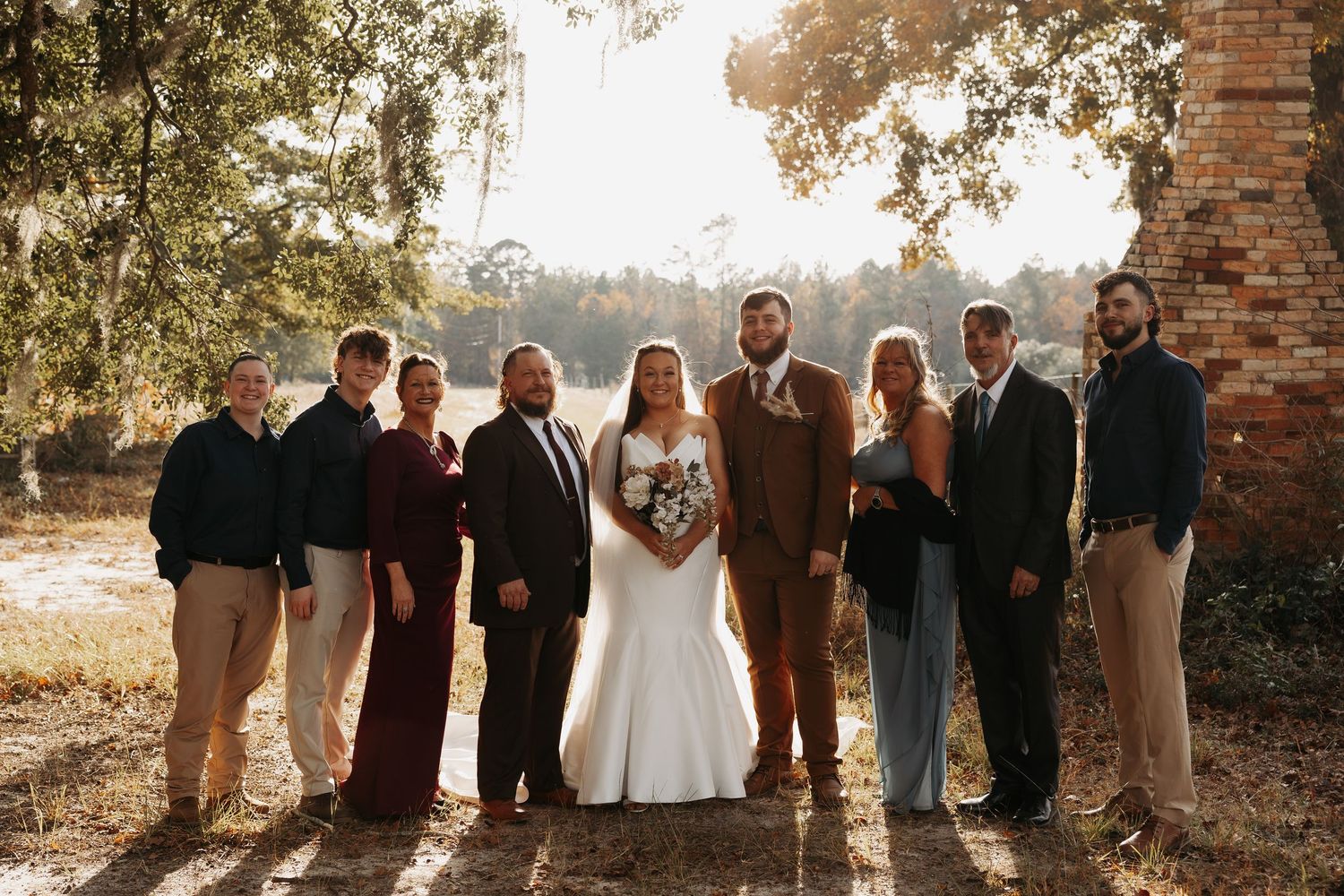 Wedding party group portrait outdoors in golden hour light at rustic venue.
