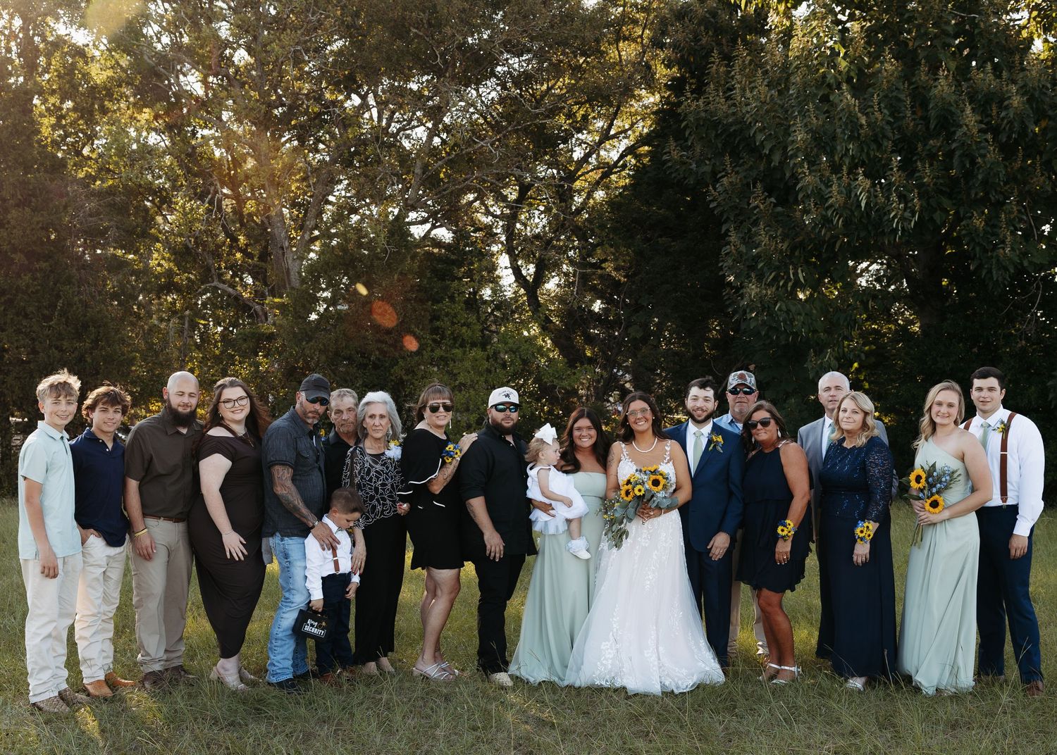 Wedding party group photo outdoors with bride in white gown holding bouquet.