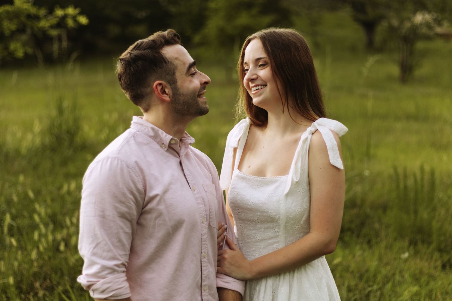 A couple shares a joyful moment together while standing in a sunny meadow surrounded by lush greenery.