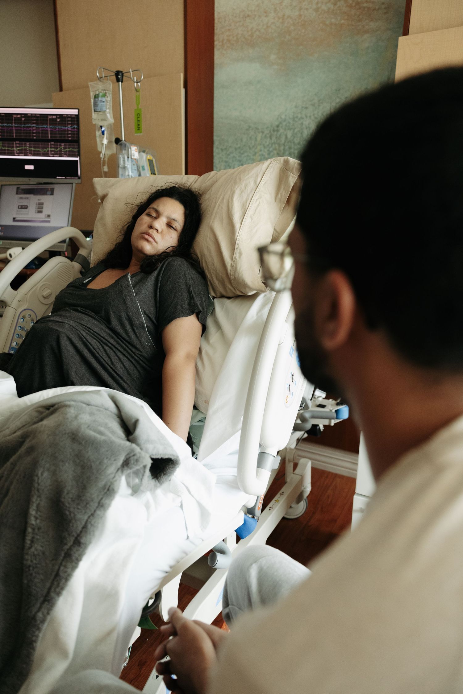 Patient lying in hospital bed while being examined by medical staff and monitored with equipment.