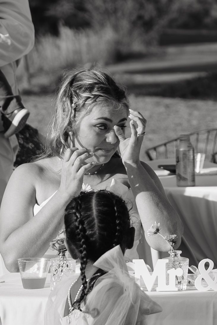 Black and white photo of an emotional bride wiping tears at wedding reception table with Mr & sign visible.