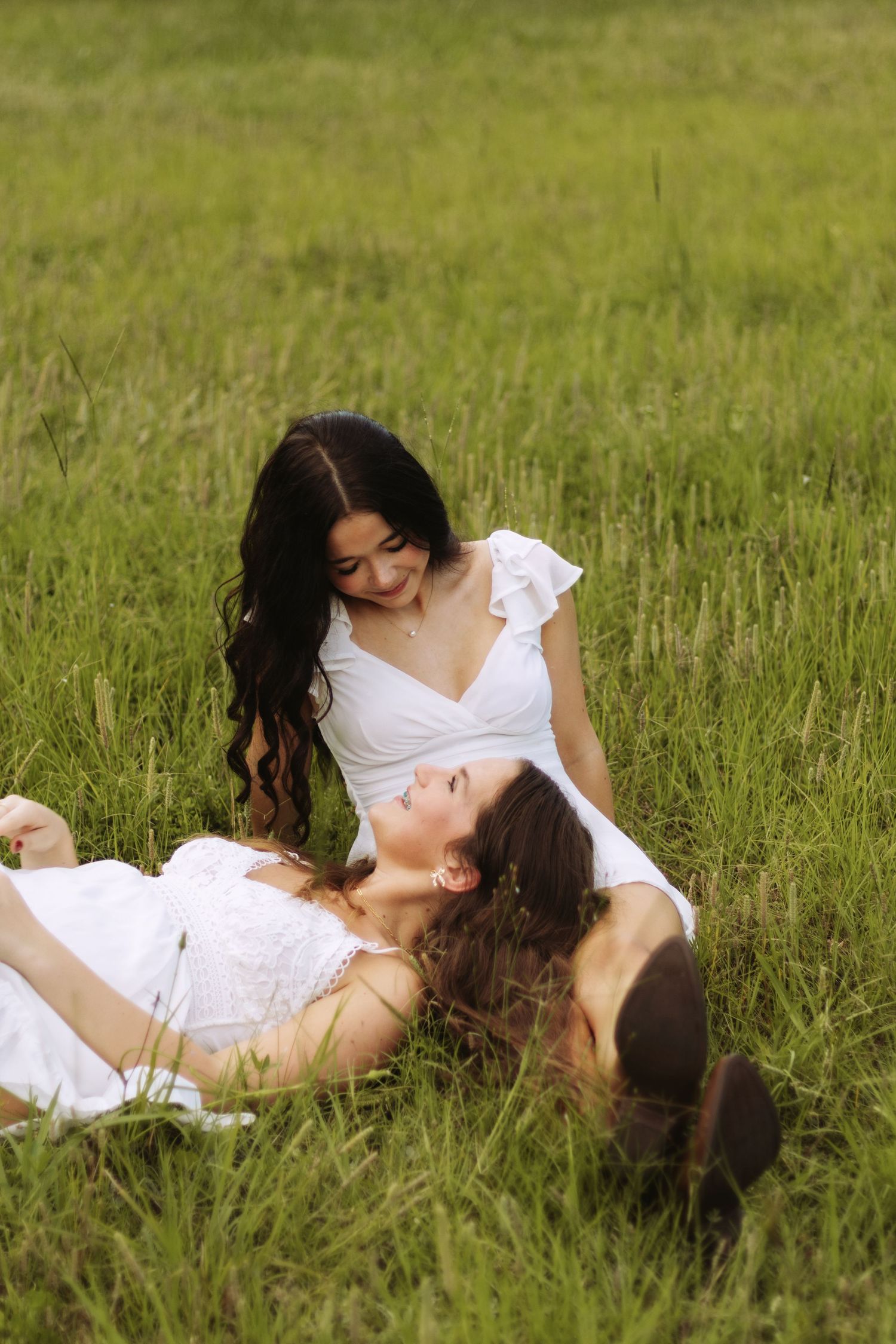 Two figures in white dresses lay together in a grassy meadow creating a romantic scene in natural light.