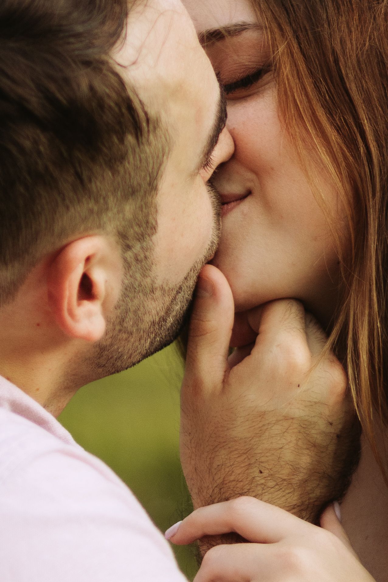 A tender romantic moment between a couple sharing an intimate kiss outdoors in natural lighting.