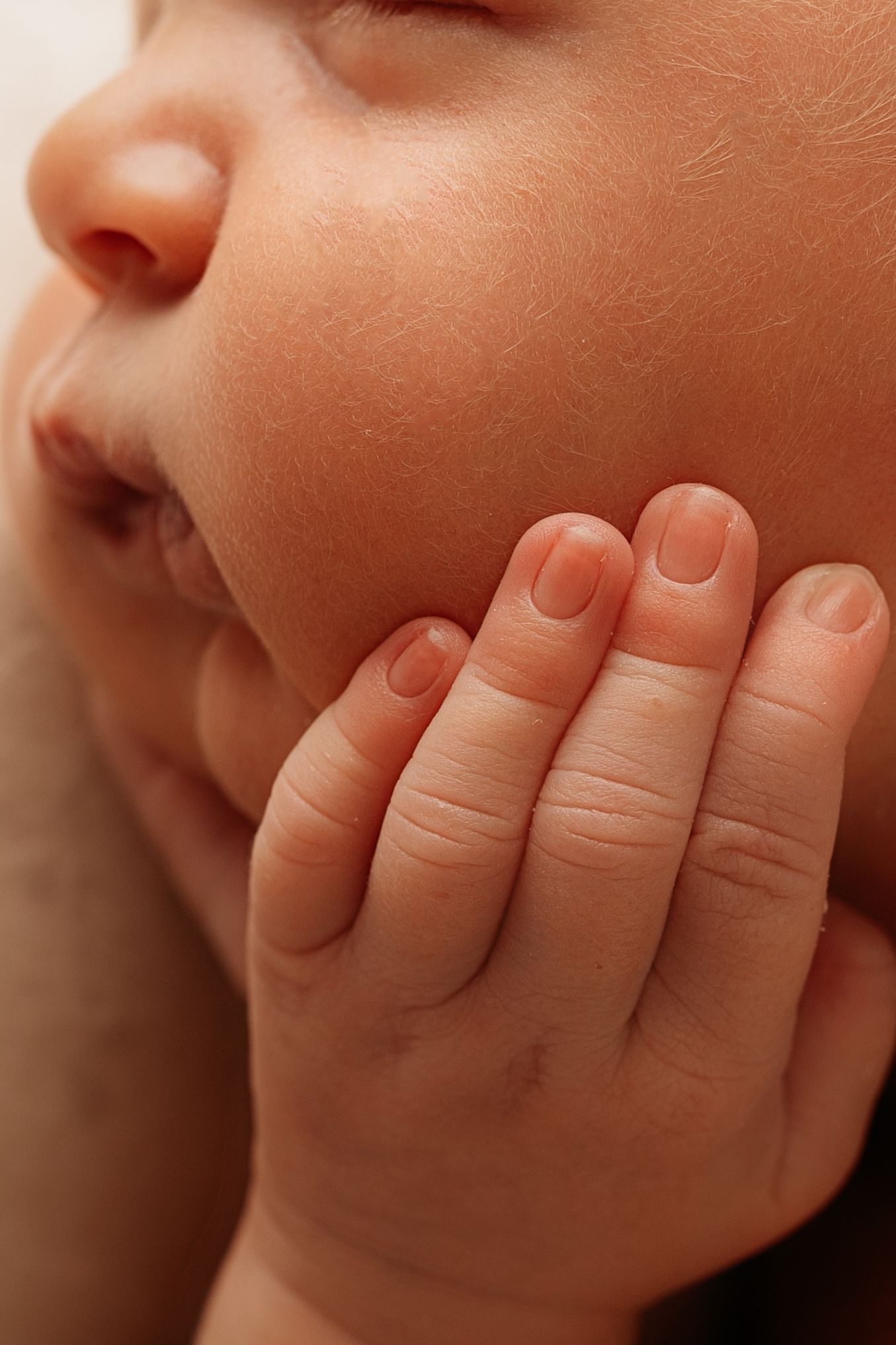 Close-up of a sleeping newborn baby's chubby cheek resting gently against their tiny delicate hand.