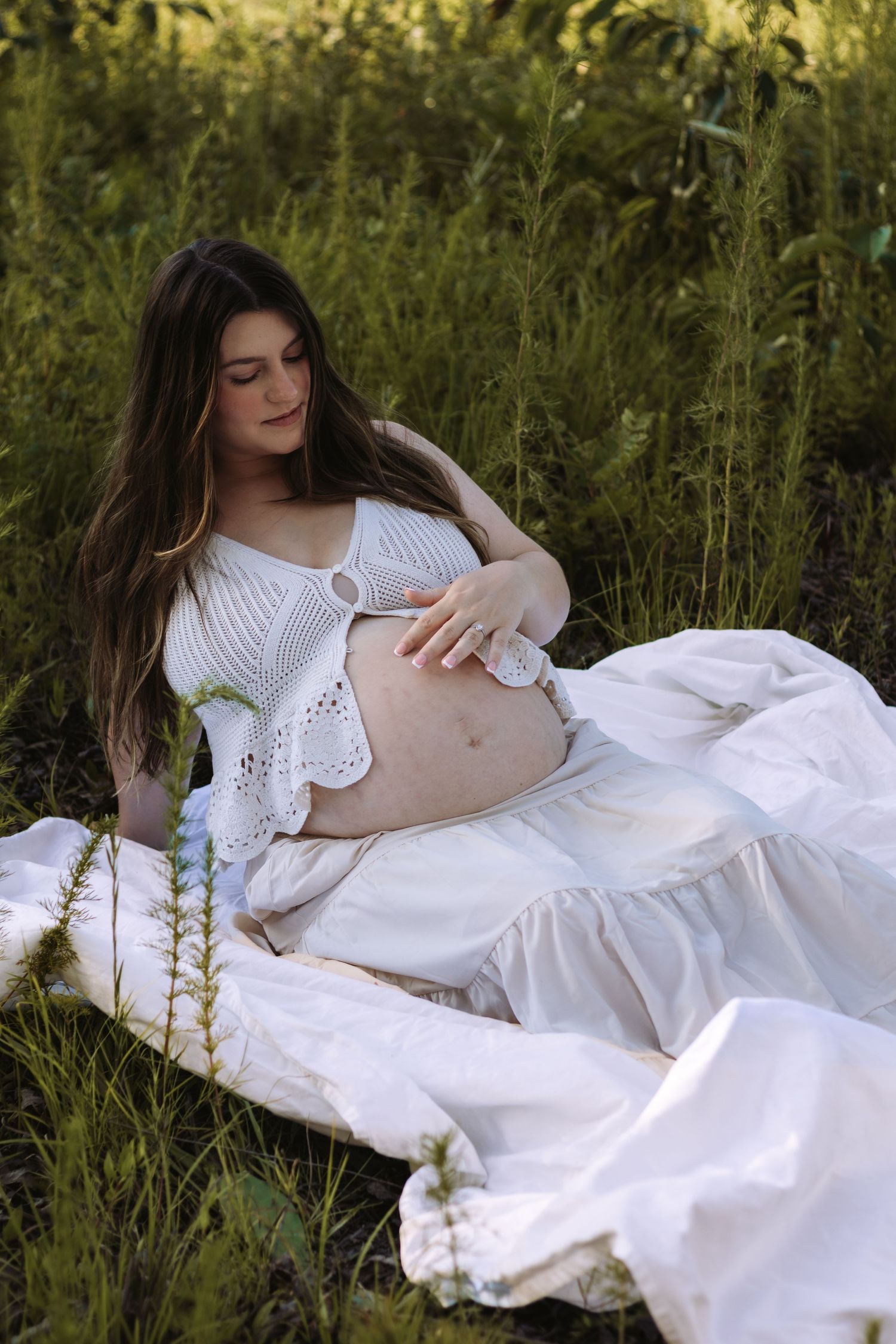 A person in a white dress lies dreamily in tall grass on a sunny afternoon.