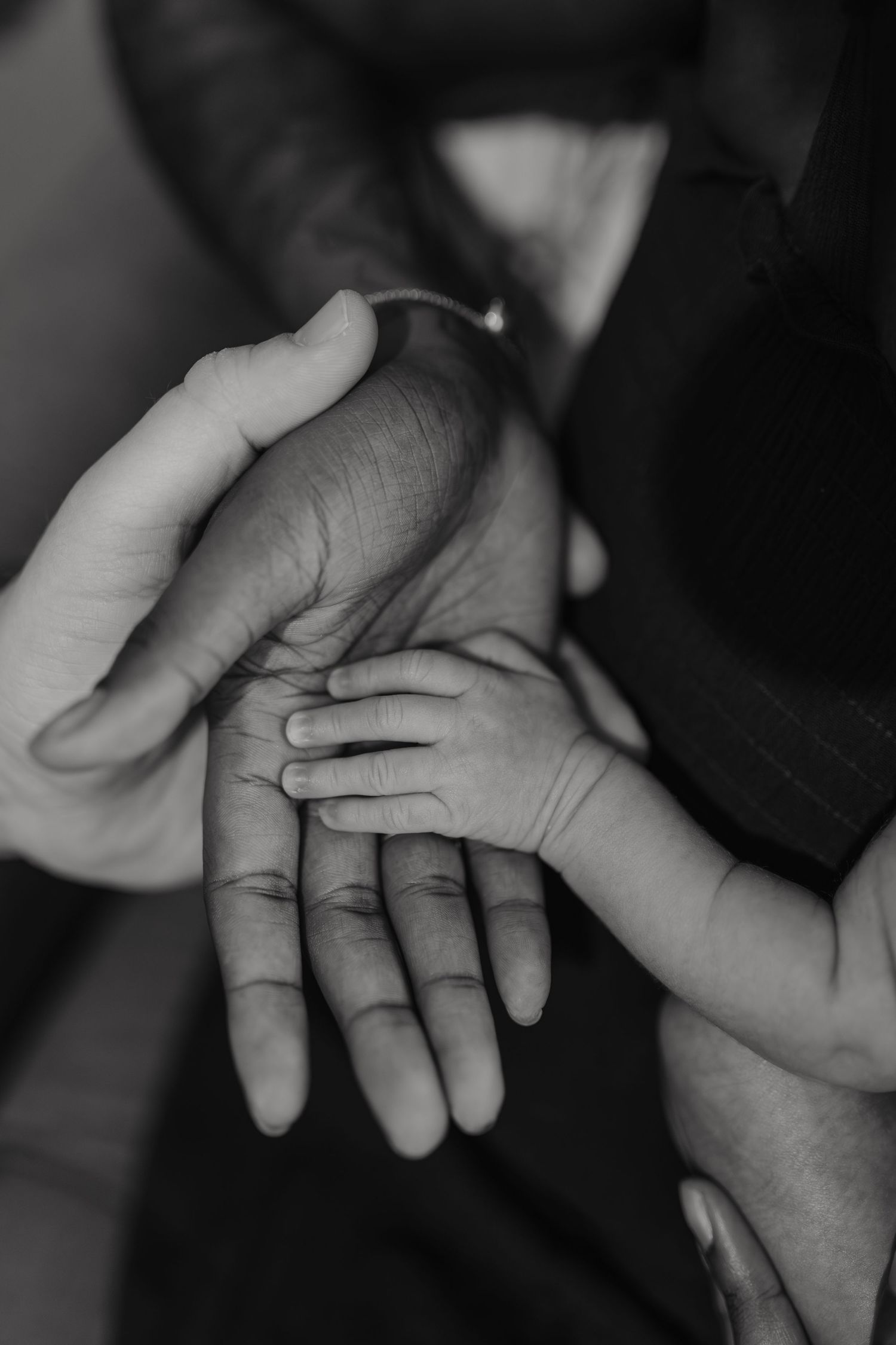 Black and white photo of a newborn baby hand resting on adult hands, symbolizing family love and new life.