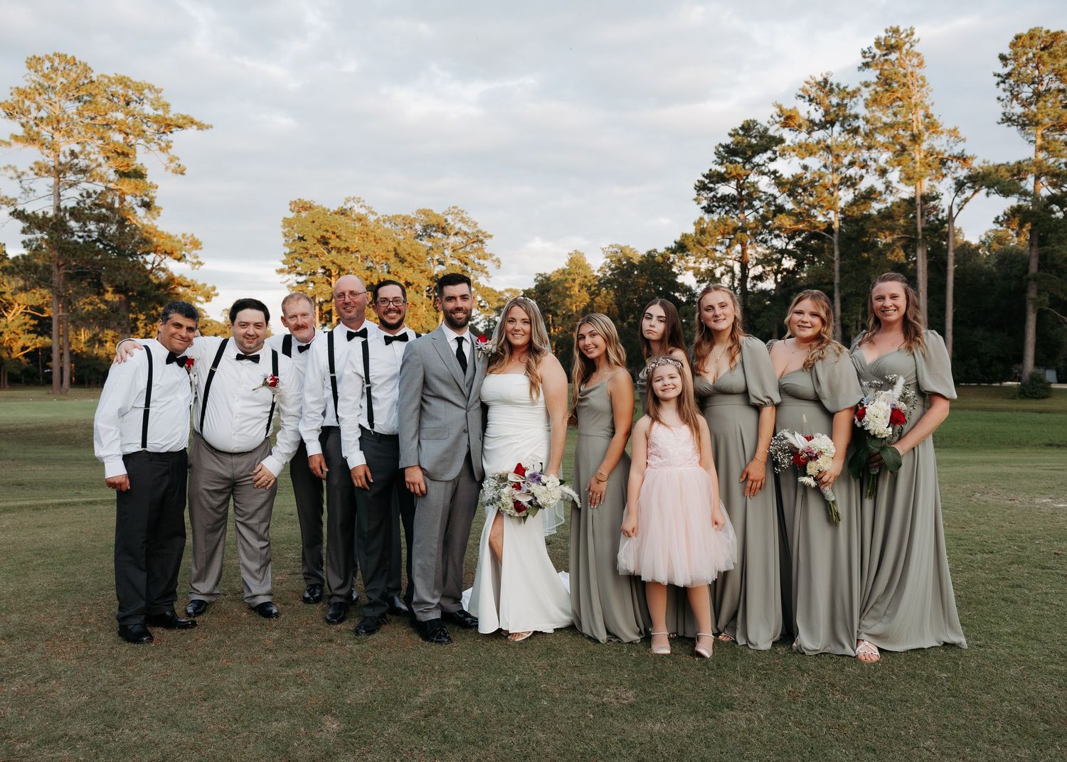 Wedding party posing outdoors on a golf course with bridesmaids in sage green dresses.