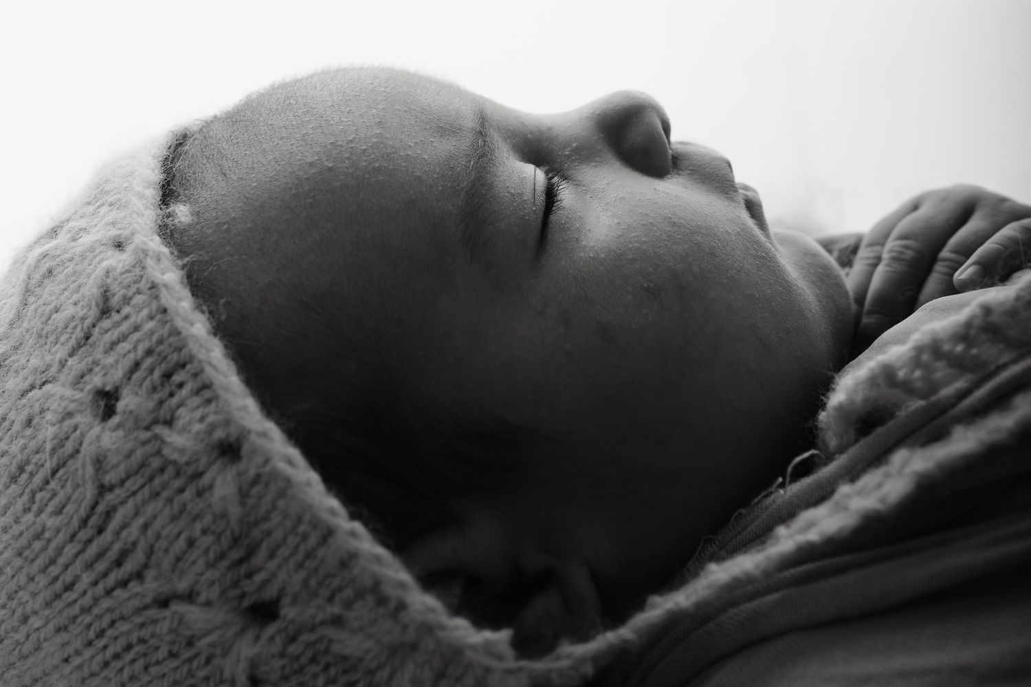 Black and white photo of a peaceful sleeping newborn baby wrapped snugly in a soft knit blanket.