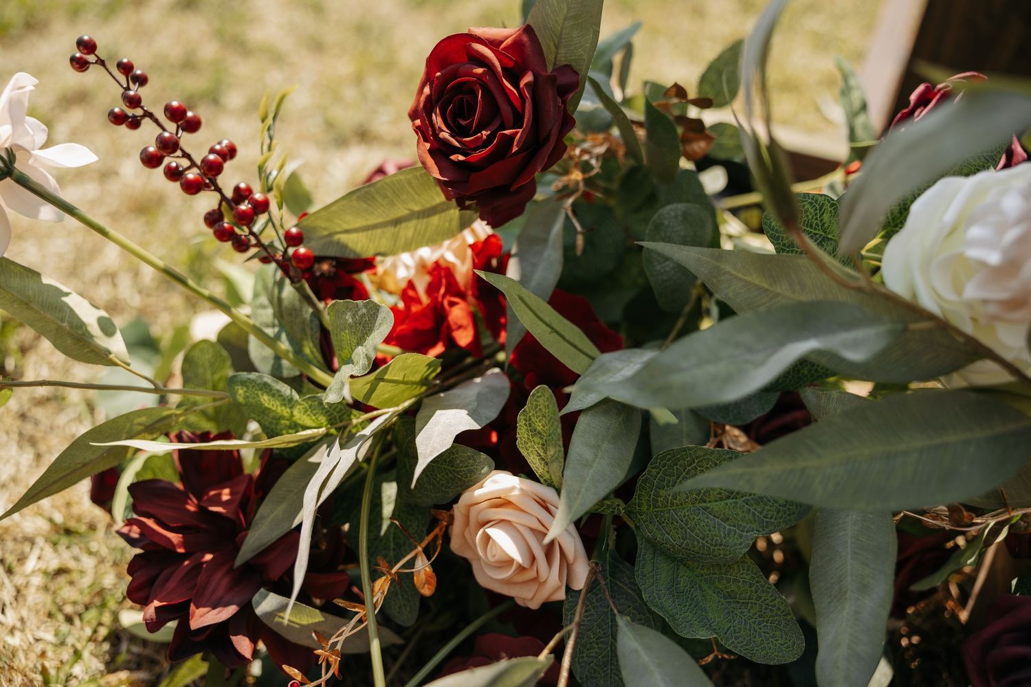 Elegant floral arrangement featuring deep red roses, blush pink flowers, burgundy blooms, and lush green eucalyptus leaves outdoors.