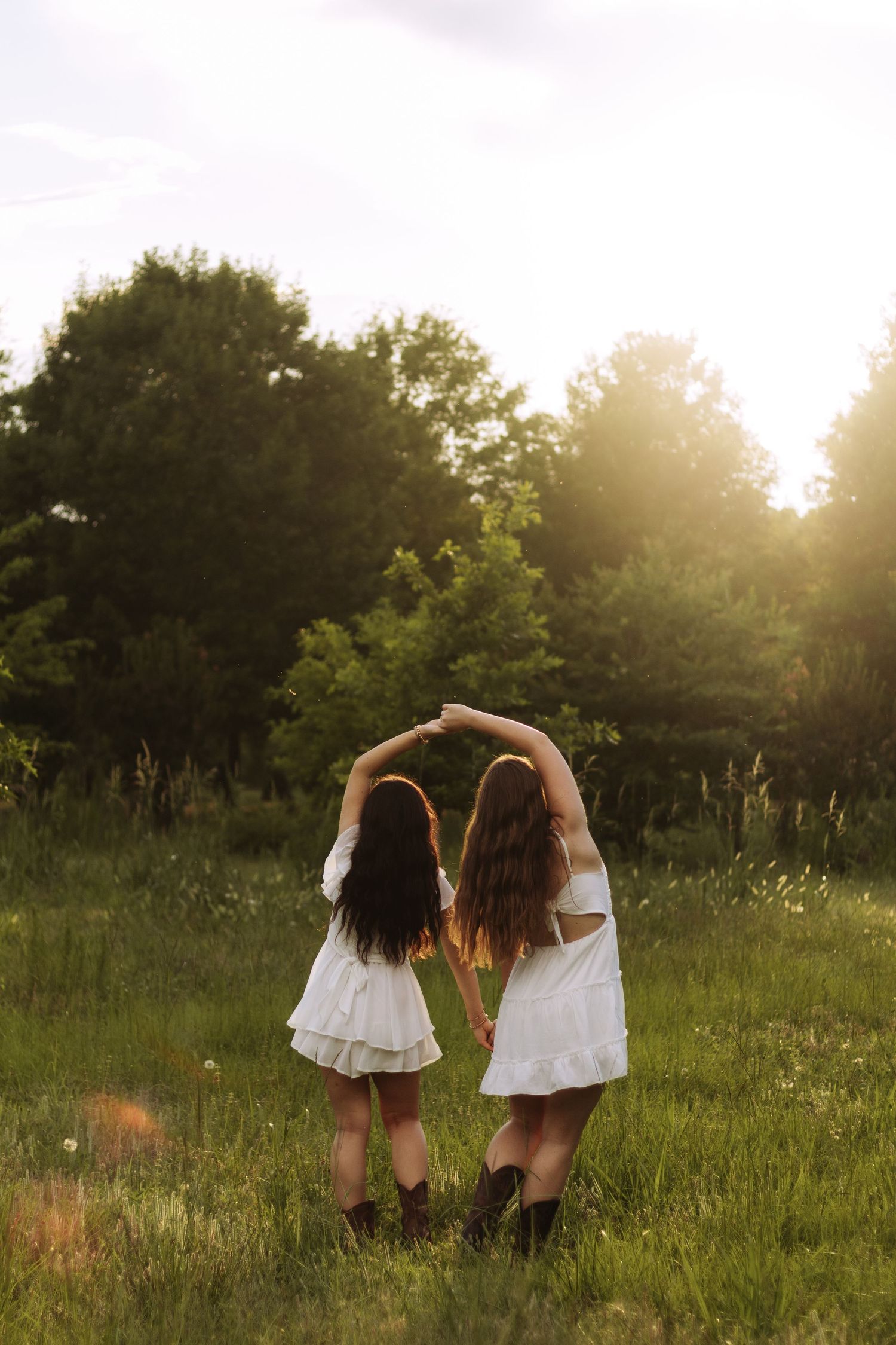 Two figures in white dresses walk through a sunlit meadow at golden hour, creating a dreamy summer scene.
