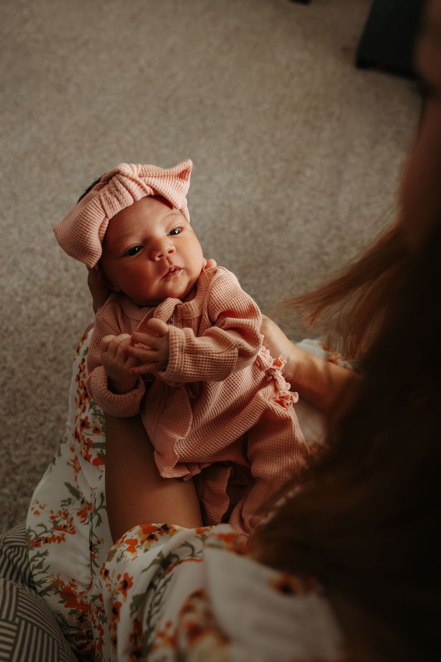 A newborn baby wearing a pink outfit is cradled in someone's arms in a series of intimate indoor portraits.