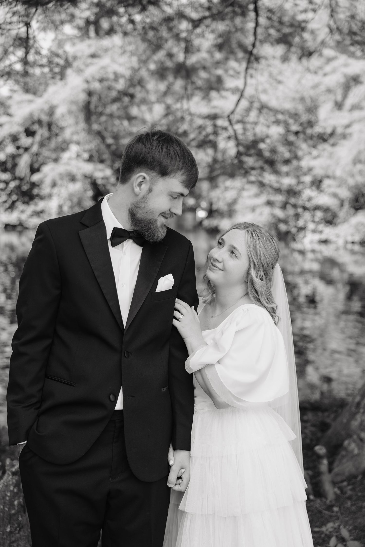 Black and white portrait of bride and groom gazing at each other in a garden.
