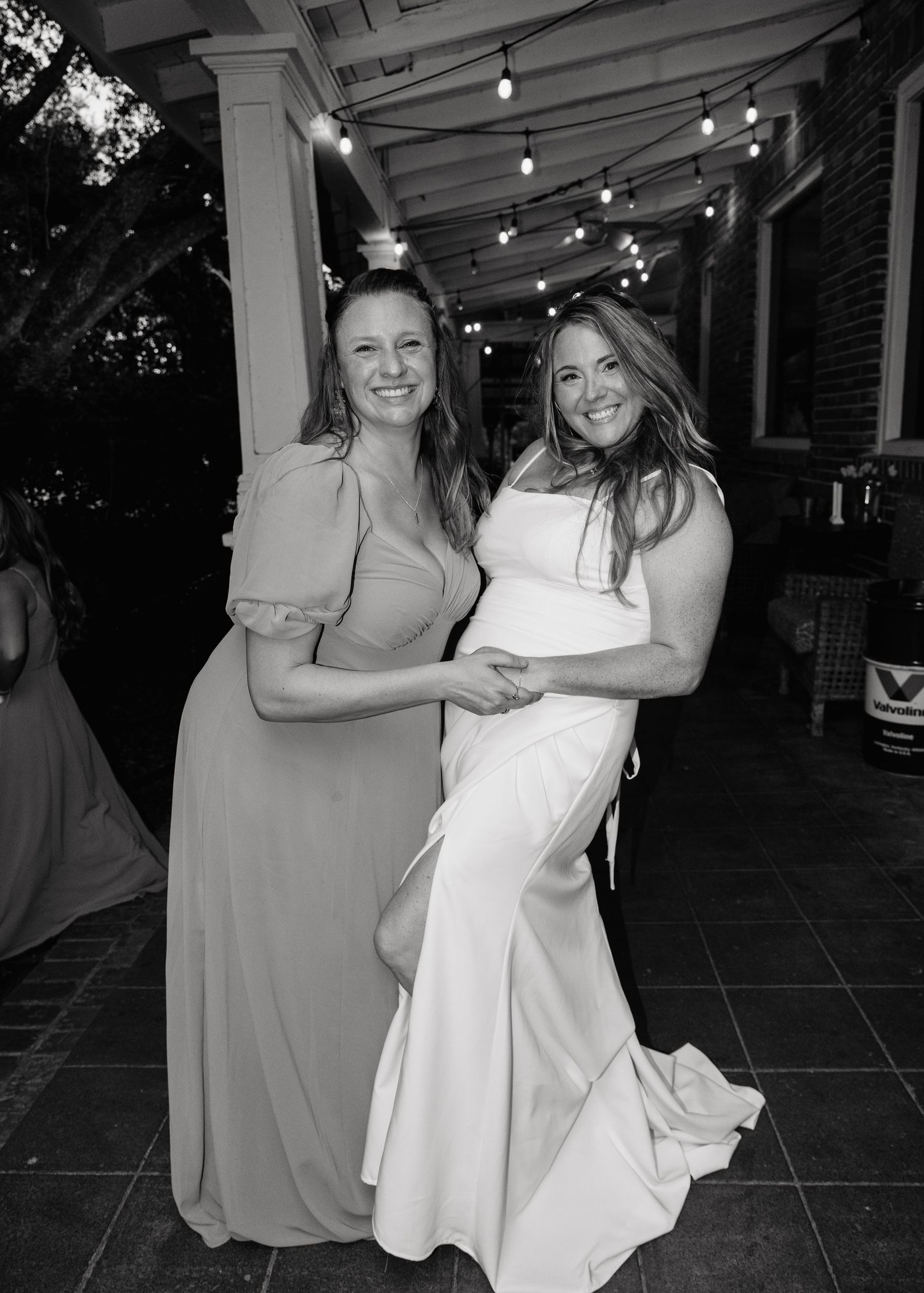 Black and white photo of two women smiling together at a wedding reception under string lights.