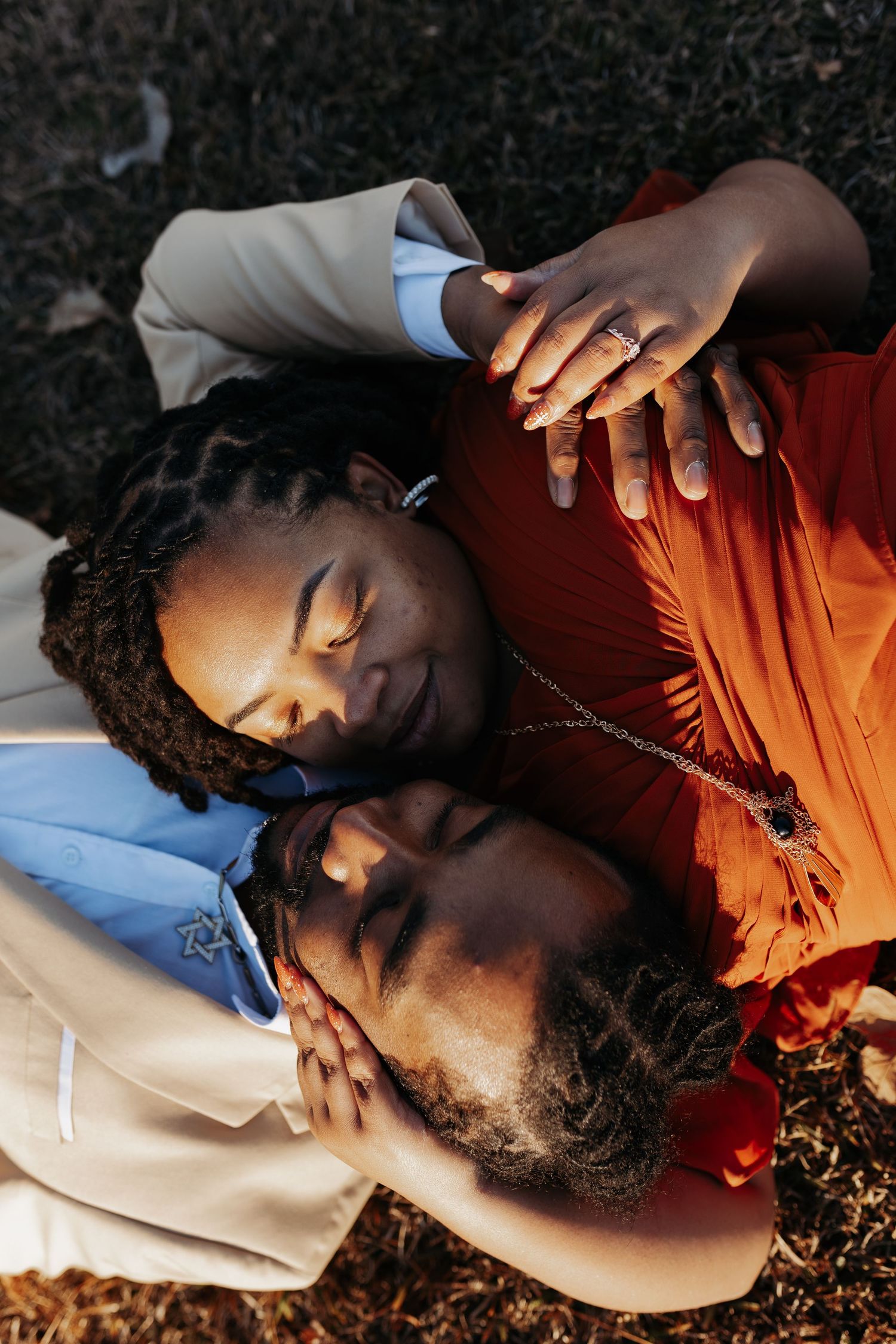 Aerial view of a couple lying on the ground, heads together, holding hands in warm sunlight.