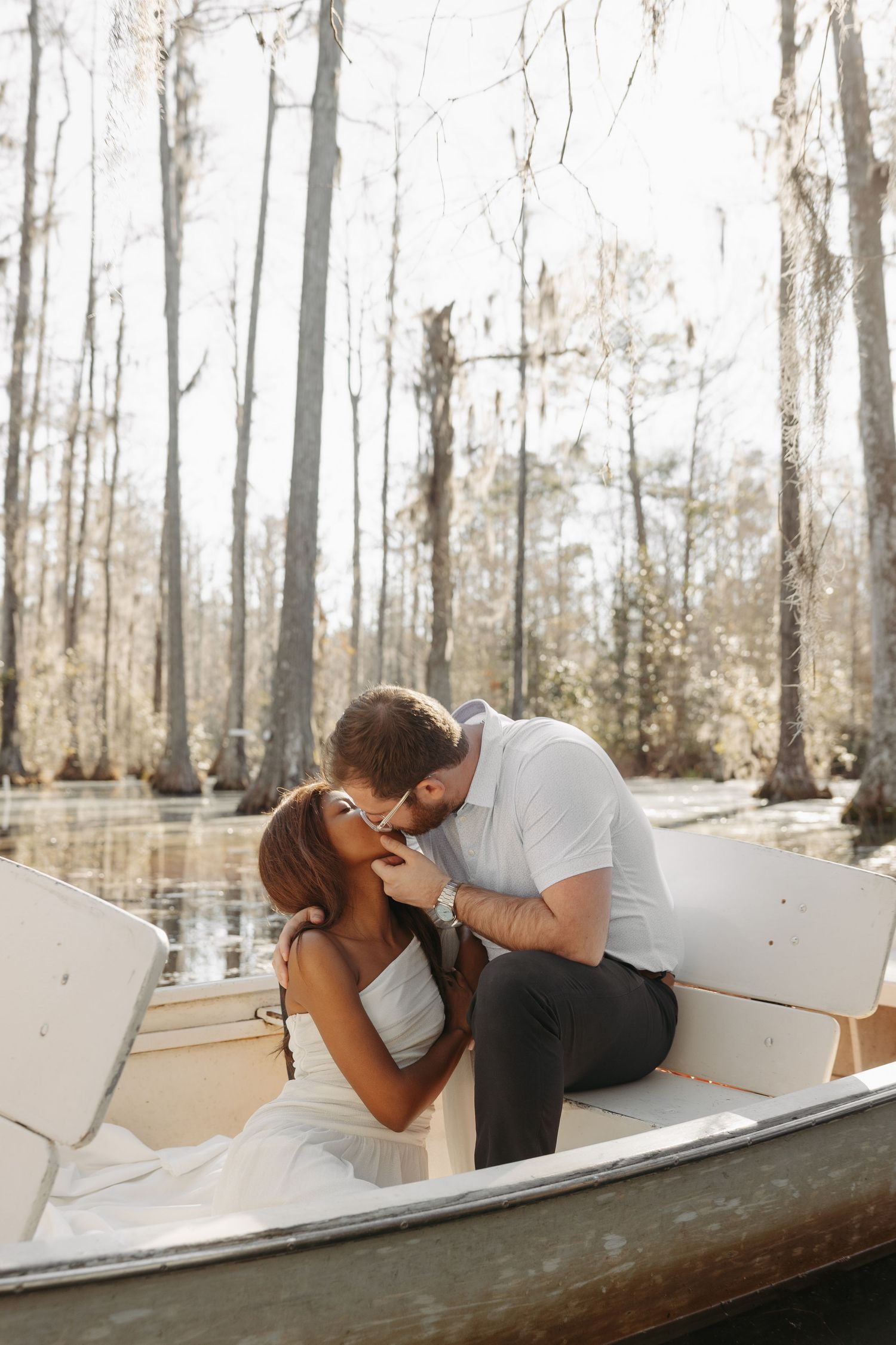 A couple shares a romantic kiss in a boat surrounded by a serene swamp forest backdrop.