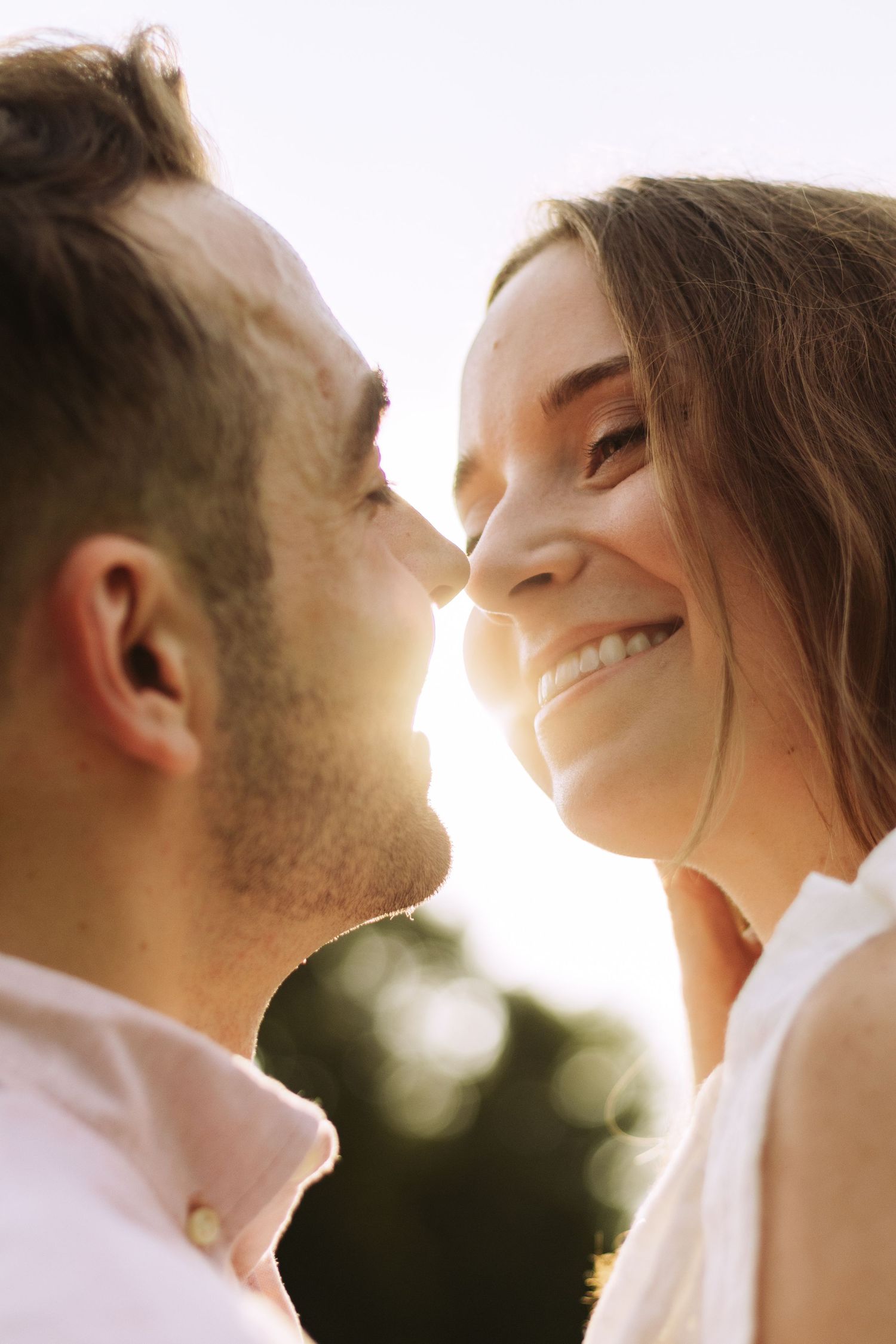 A romantic couple share a tender moment in warm sunlight while wearing white clothing.