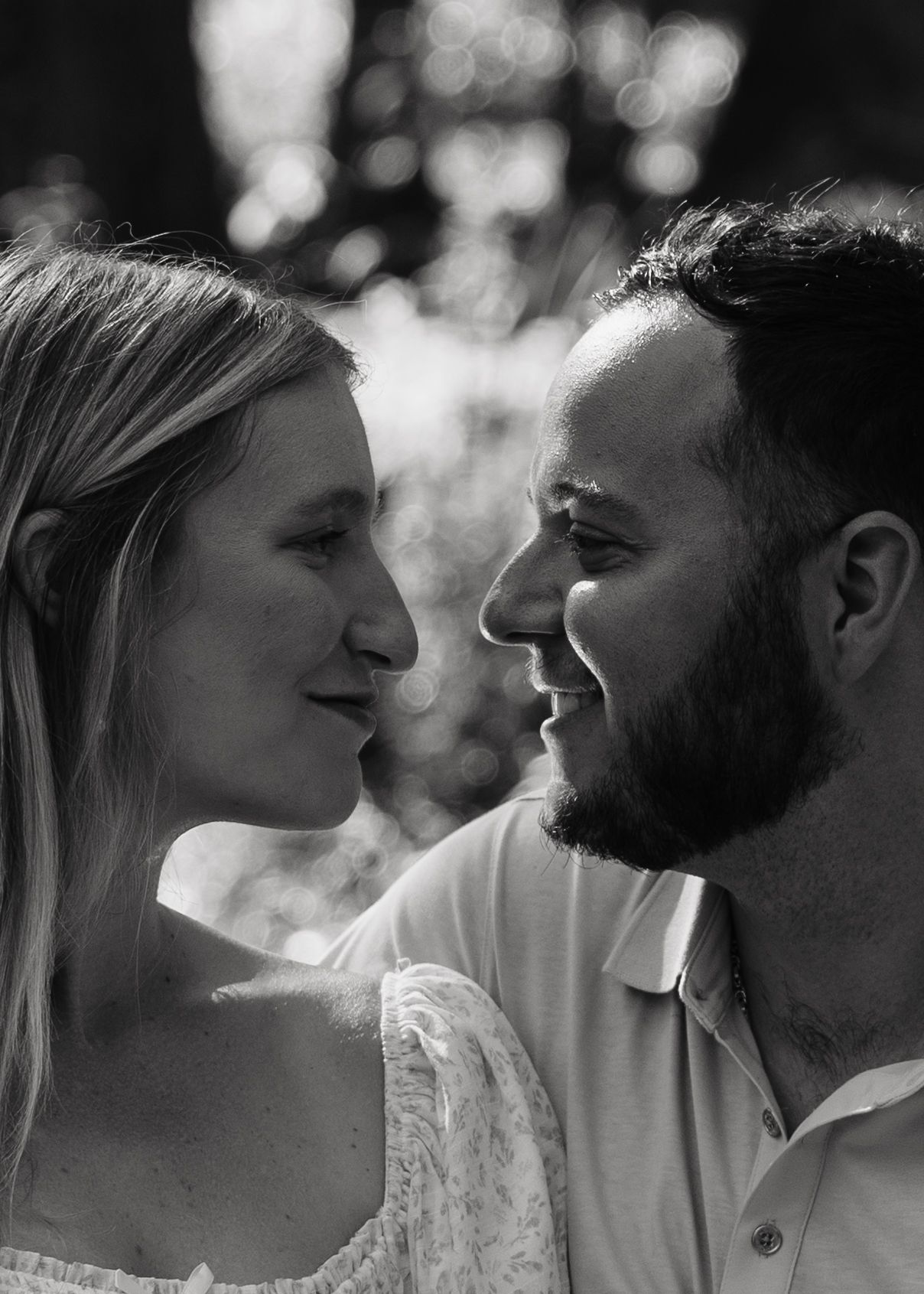 Black and white portrait of a smiling couple gazing at each other outdoors in soft natural light.