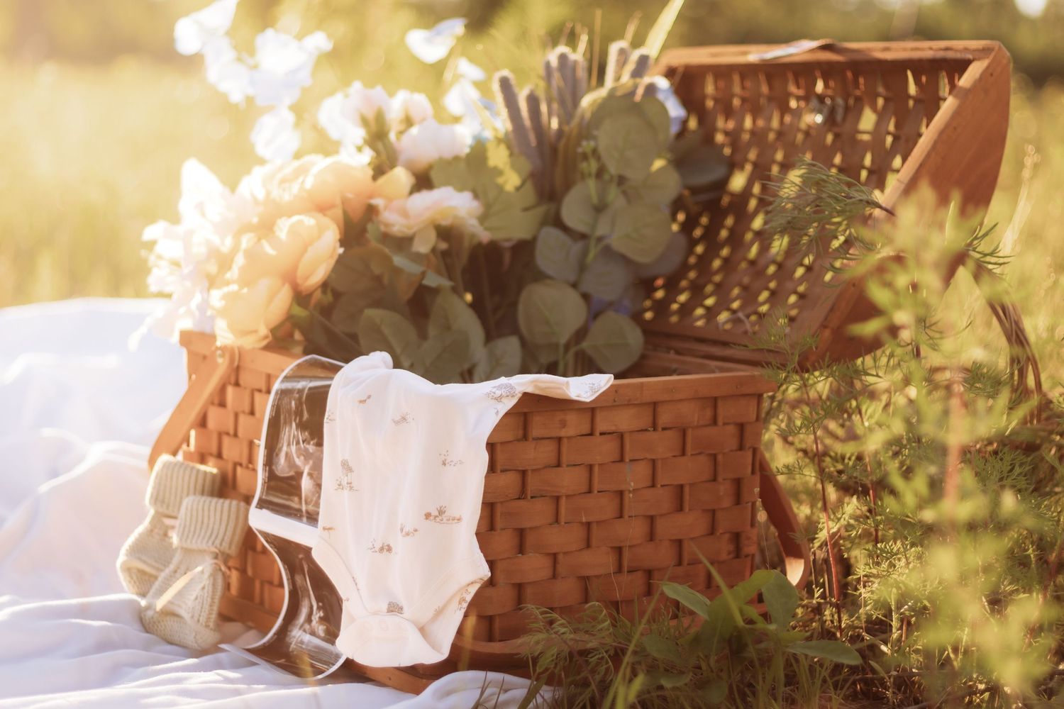 Wicker picnic basket with flowers and baby items in warm sunset light.