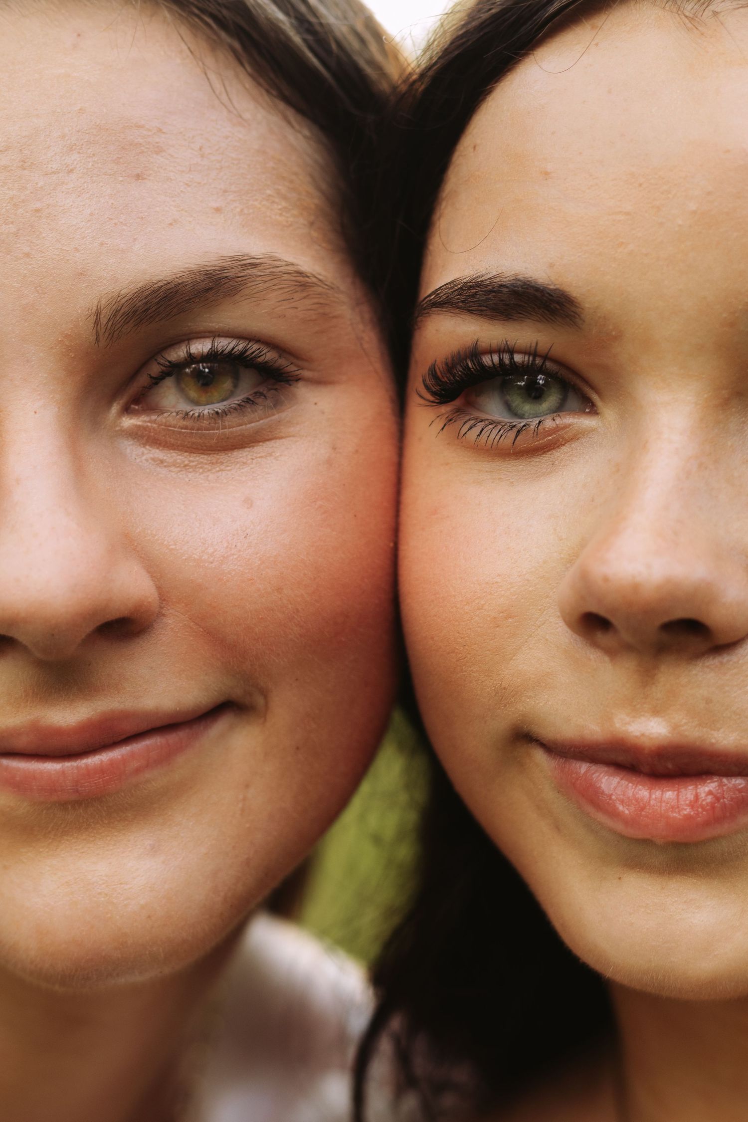 Close-up portrait of two friends with bright eyes and gentle smiles pressing their faces together.