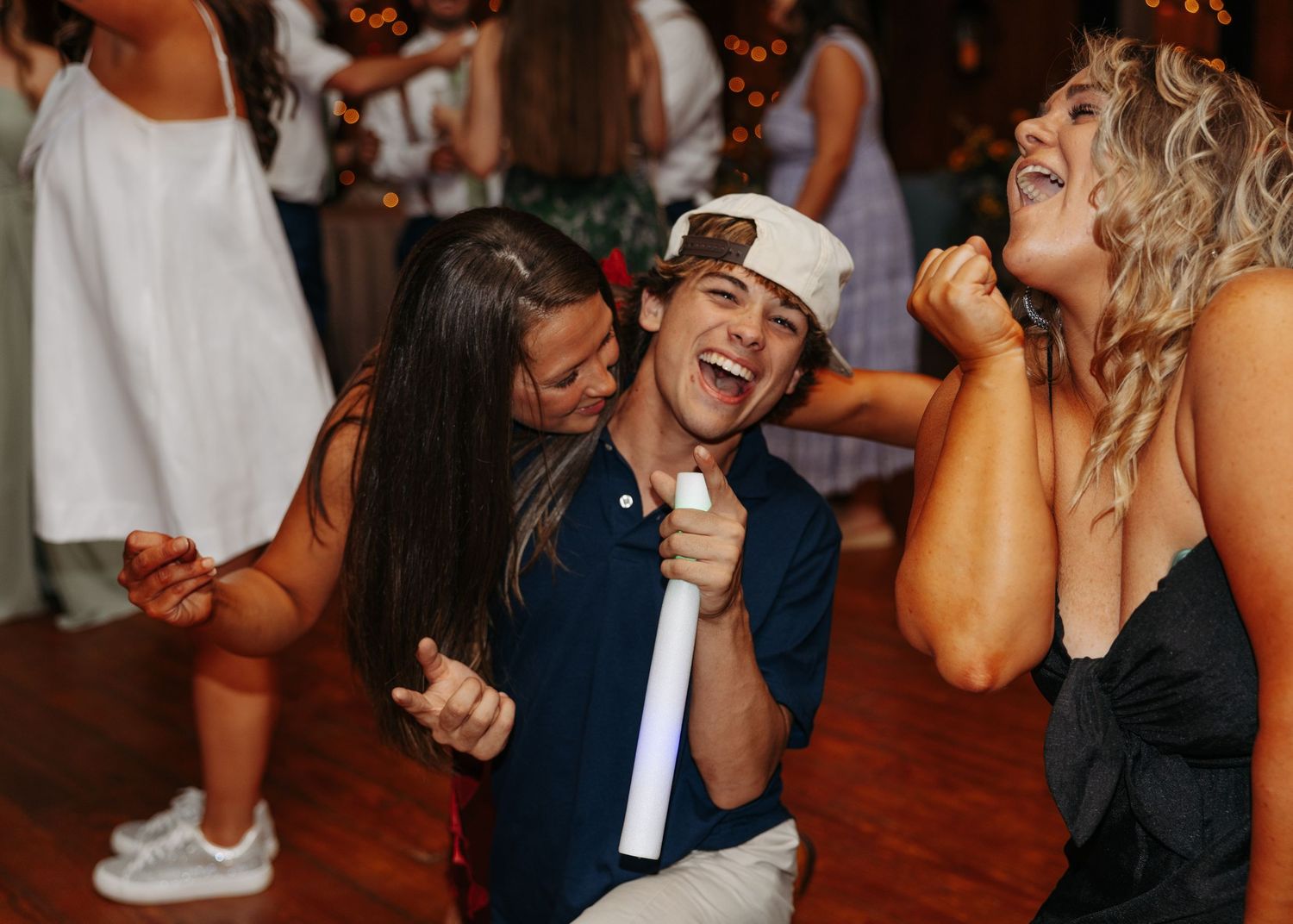 Young man laughing and dancing between two women at a lively wedding reception party.
