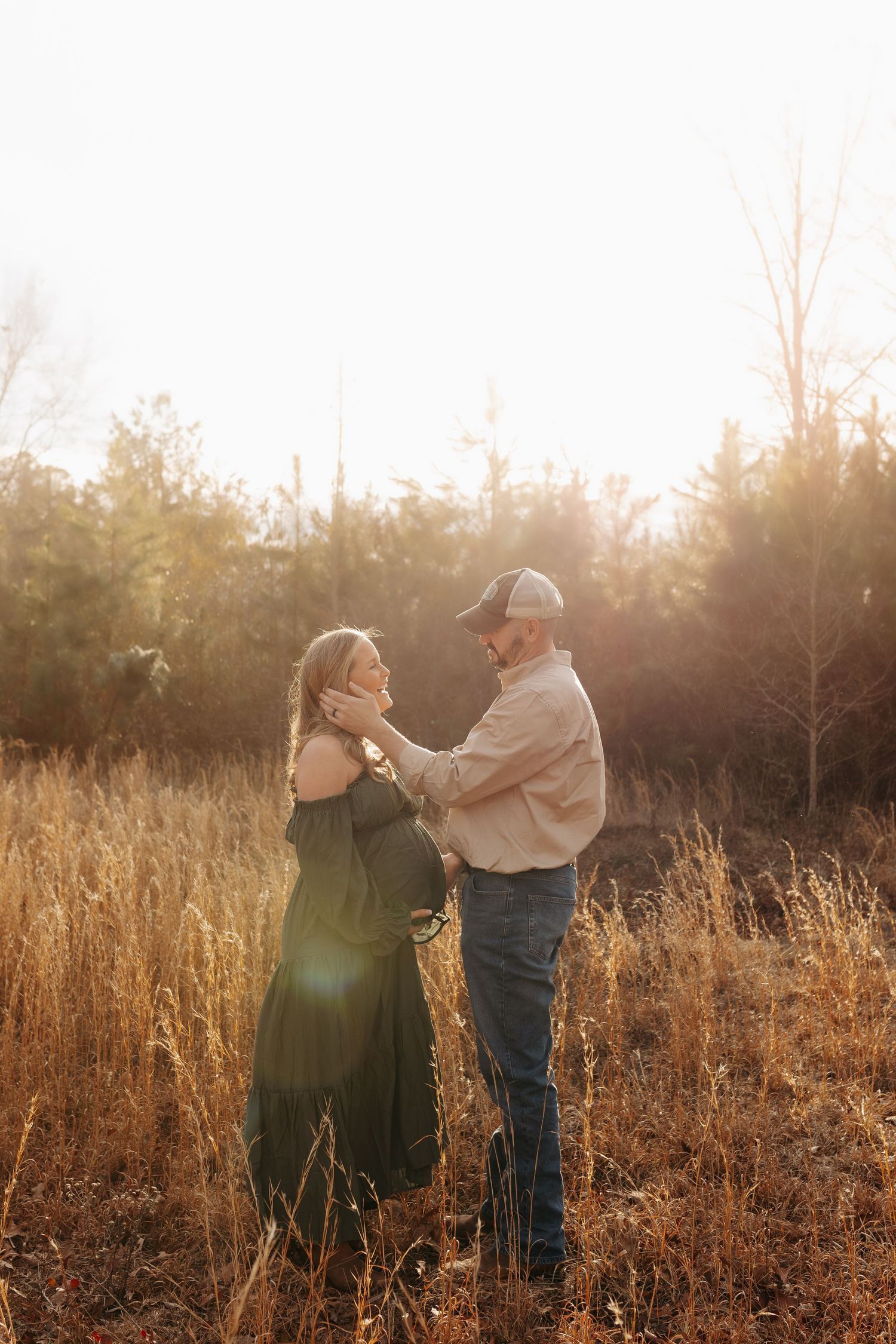 A couple embraces in a sunlit field of tall golden grass during sunset.