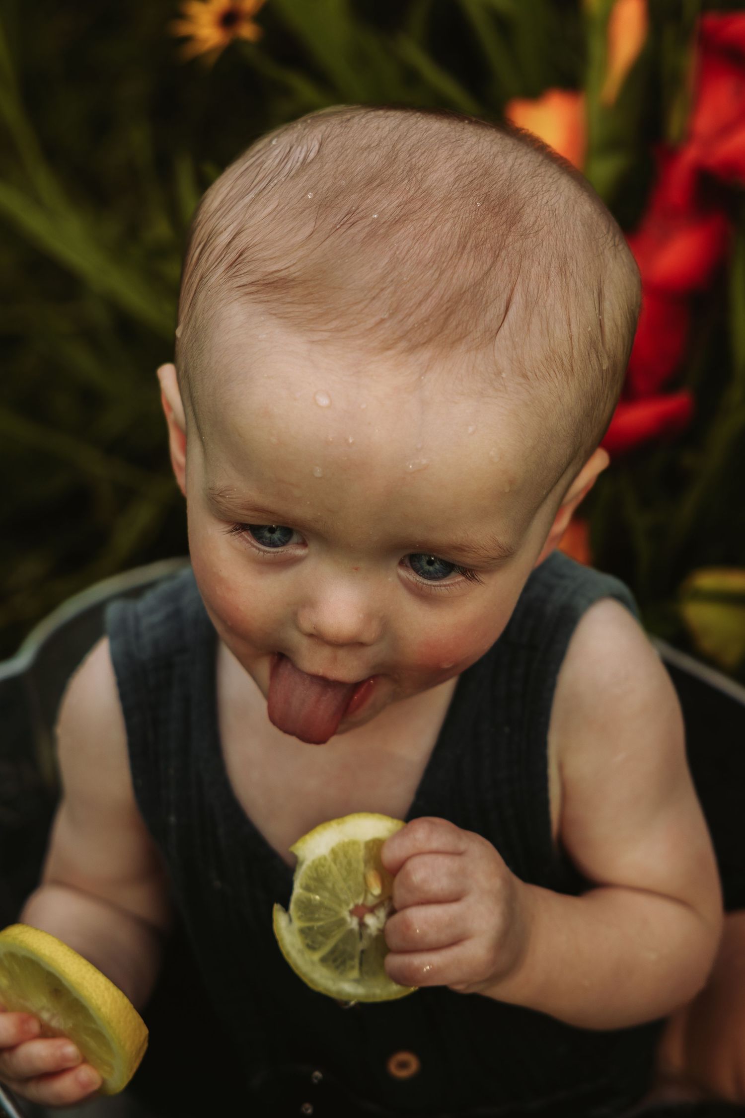 Young child in black tank top making funny faces while tasting a lemon slice.