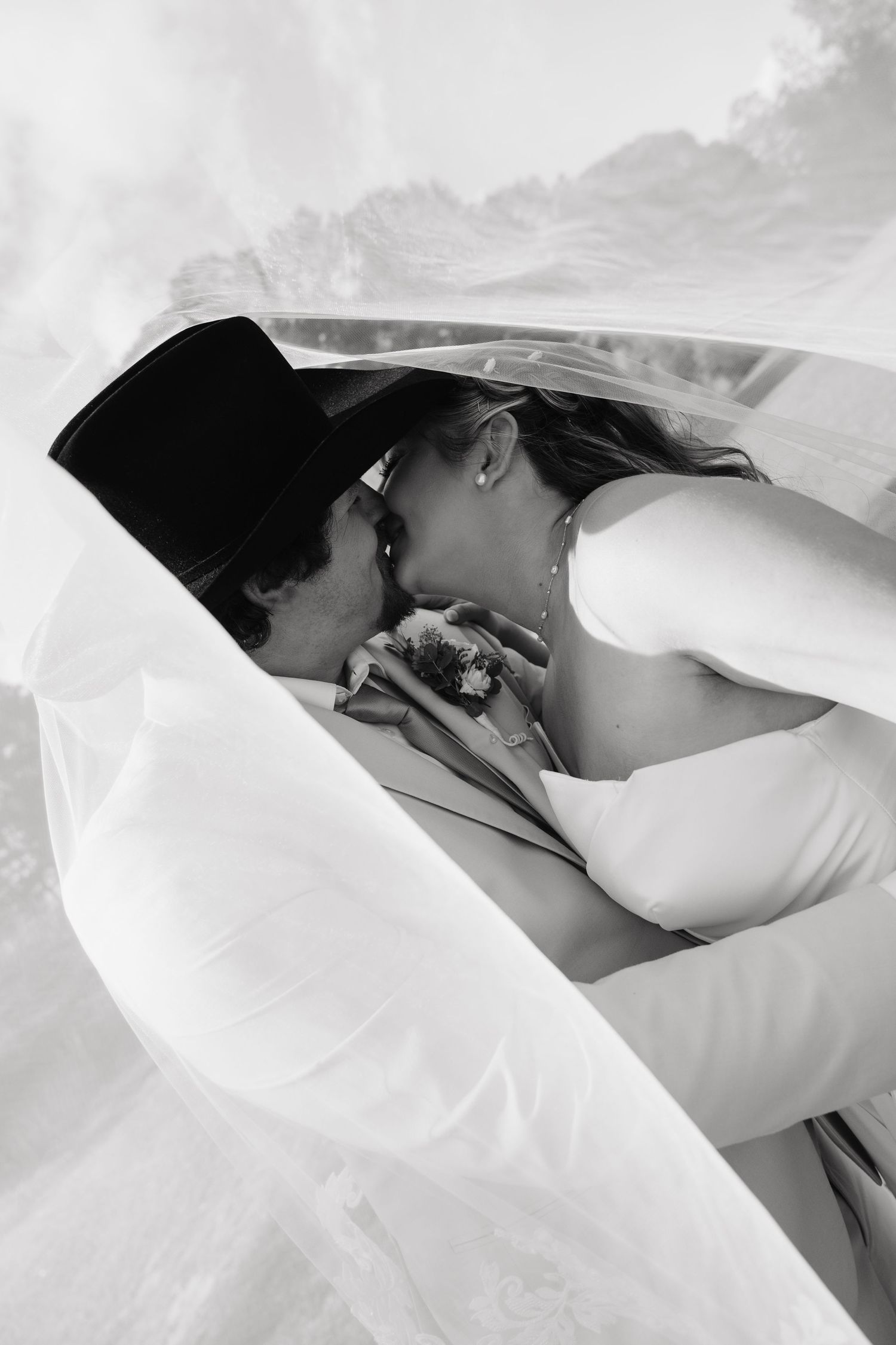 Black and white romantic photo of bride and groom kissing beneath a flowing wedding veil.