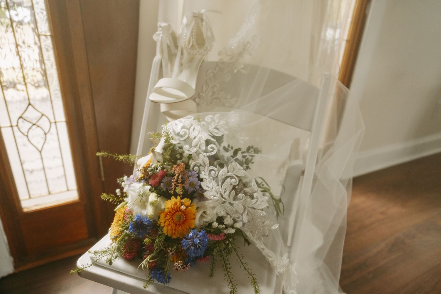 Elegant wedding dress displayed on a ladder with a colorful bridal bouquet featuring blue, yellow, and red flowers.