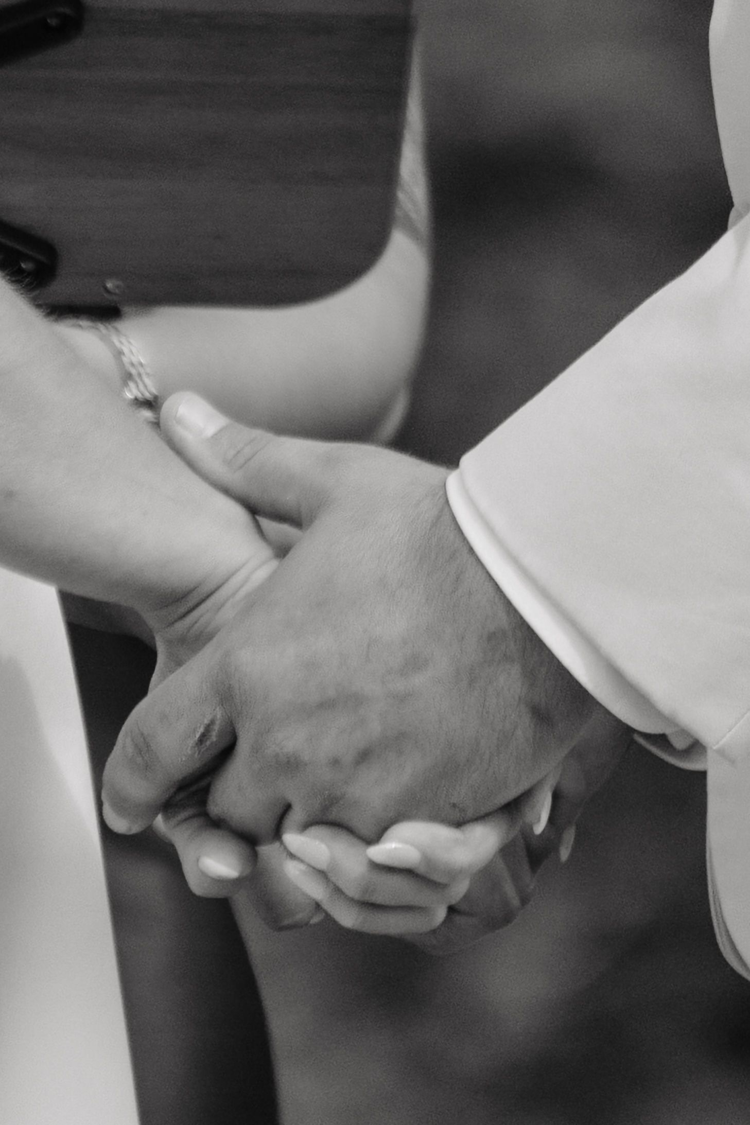 Black and white photo of a couple holding hands, showing love and unity, likely at a wedding ceremony.