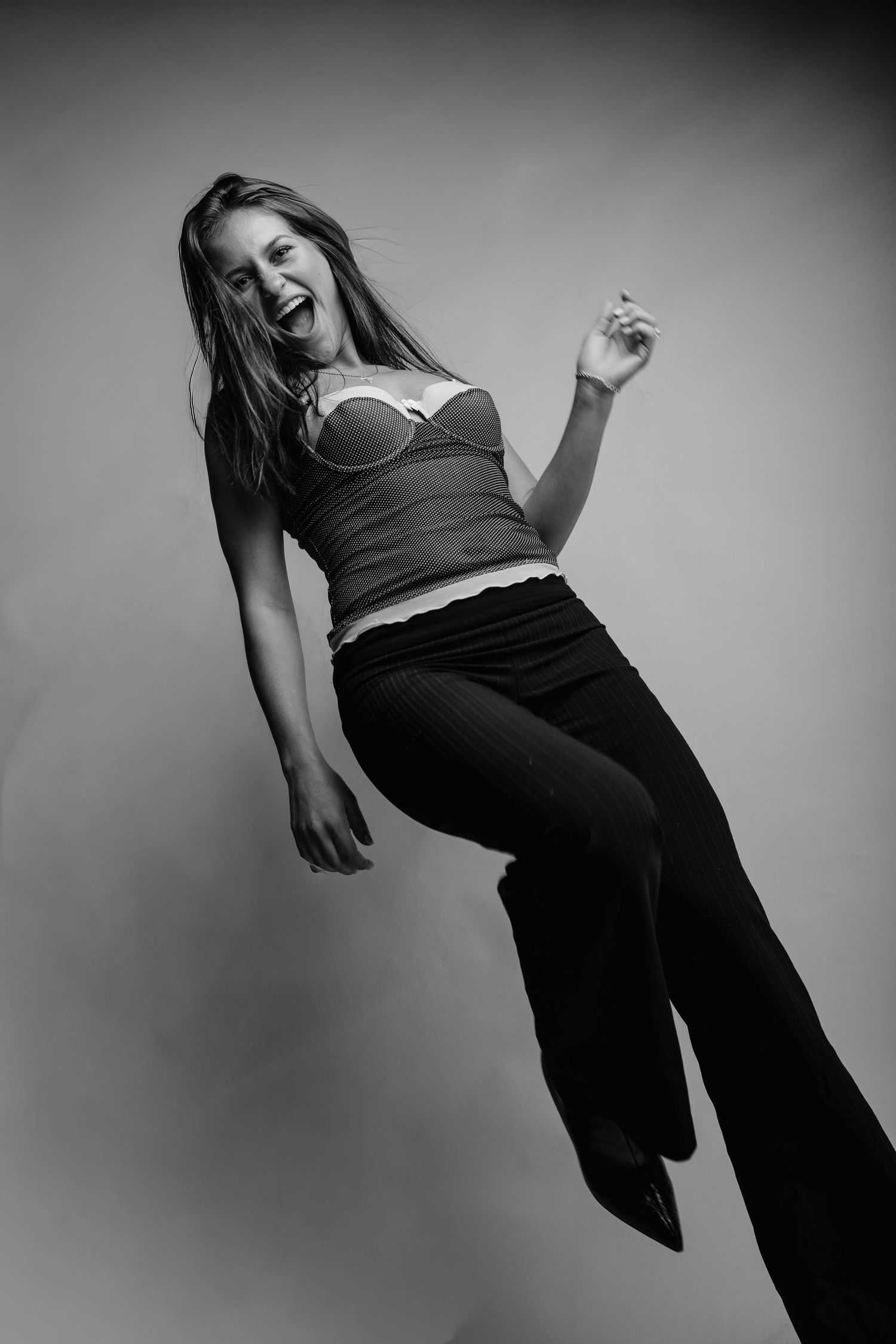 Black and white portrait of someone dancing joyfully in casual attire against a simple background.