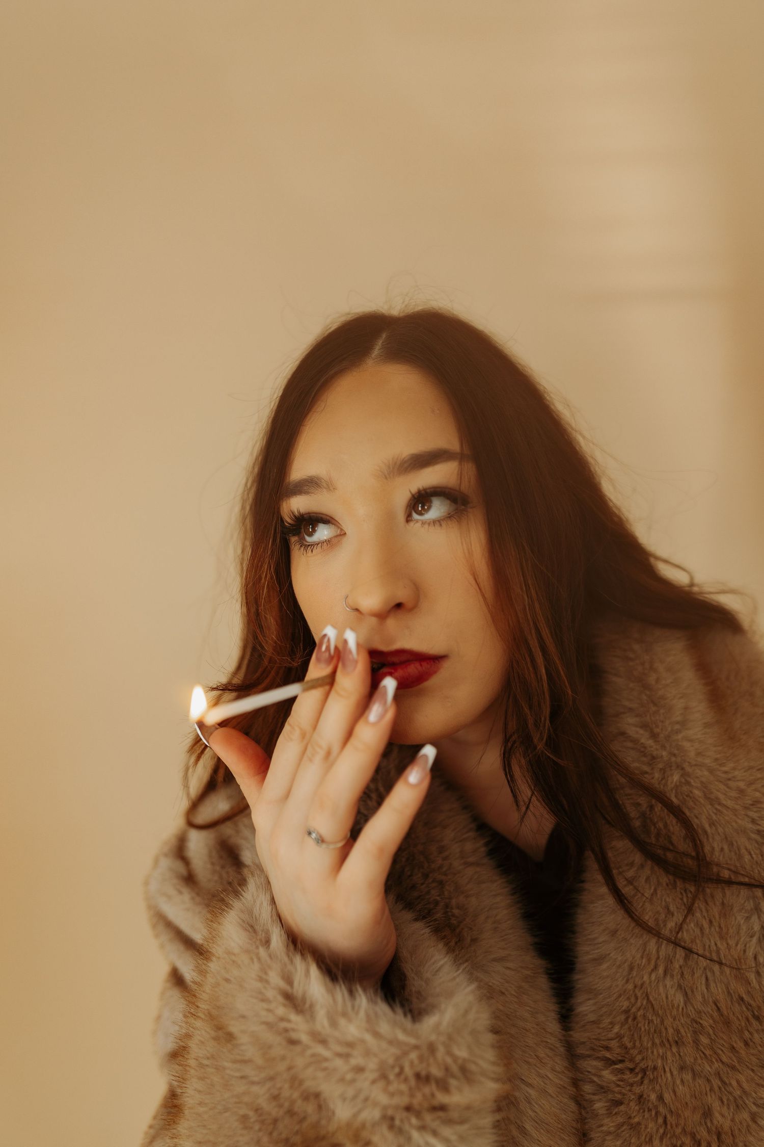 A portrait of someone in a fur coat wearing red lipstick and looking up while smoking a cigarette.