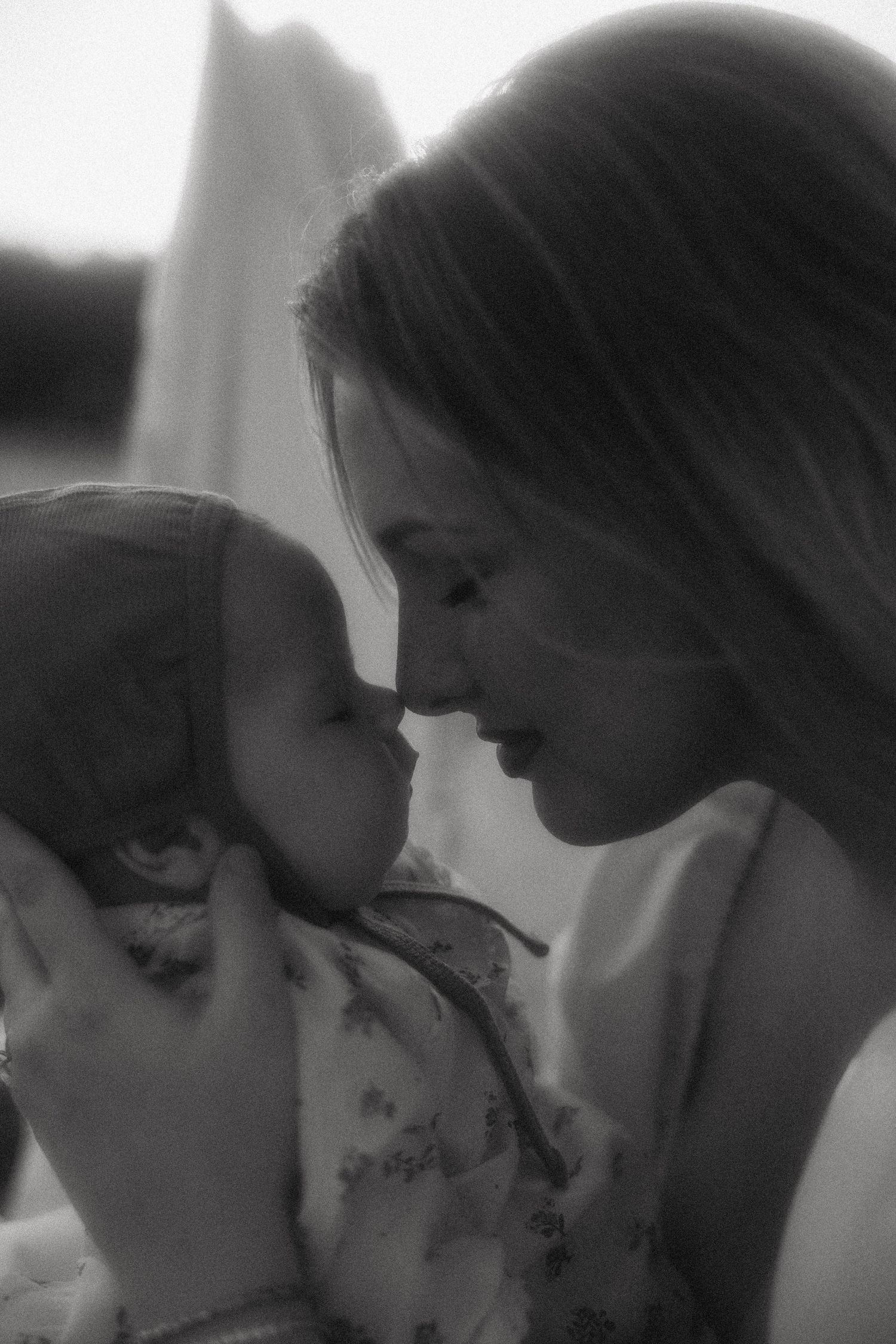 Black and white photo of a mother tenderly touching noses with her smiling baby in a loving moment.