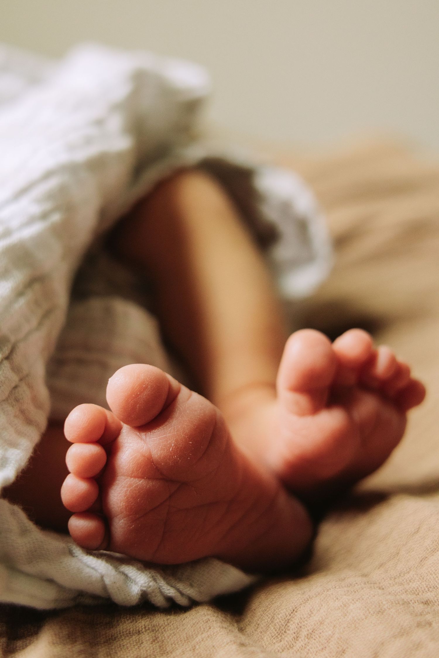 Close-up shots of tiny newborn baby feet wrapped in soft white blanket on beige textured surface.