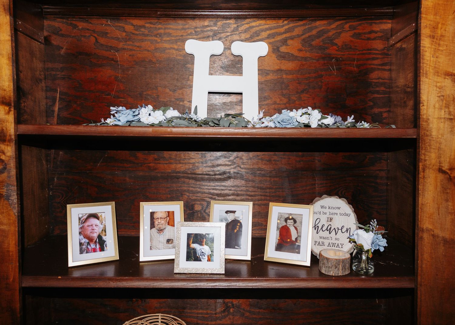 Wooden bookshelf displaying framed family photos under decorative letter H.