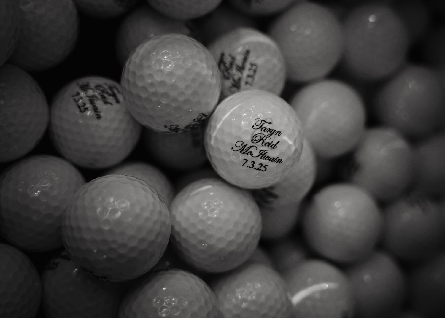 Close-up of personalized wedding golf balls with custom text, surrounded by white golf balls in black and white photo.