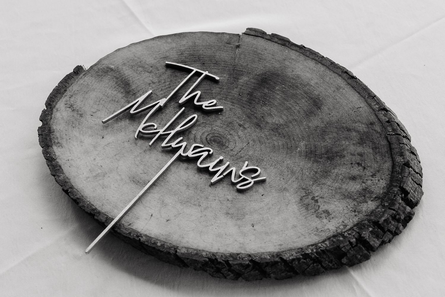 Black and white photo of a rustic wood slice sign reading The Millyans, perfect for personalized wedding decor.