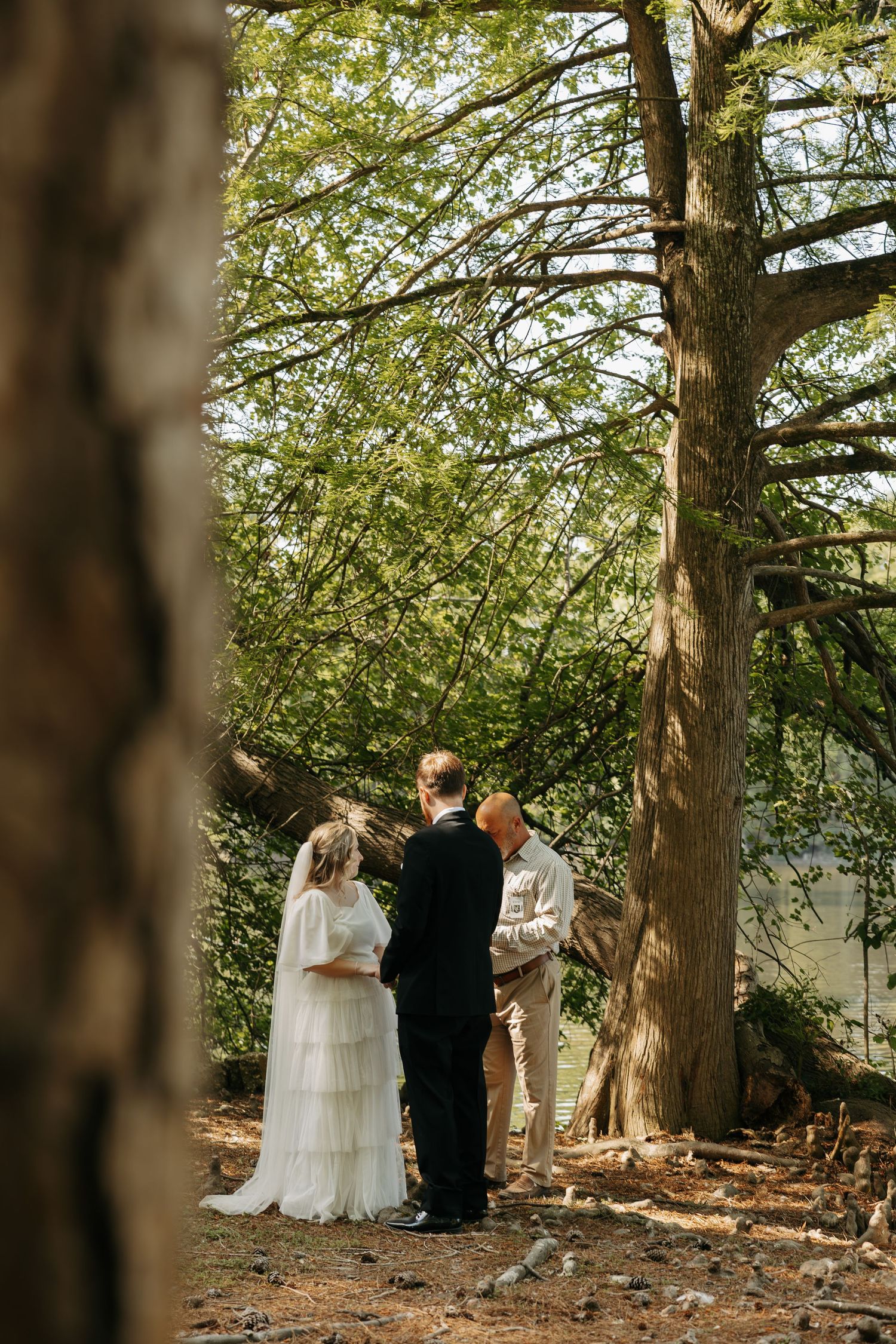 Bride and groom exchange vows with officiant in a serene forest ceremony surrounded by lush green trees.