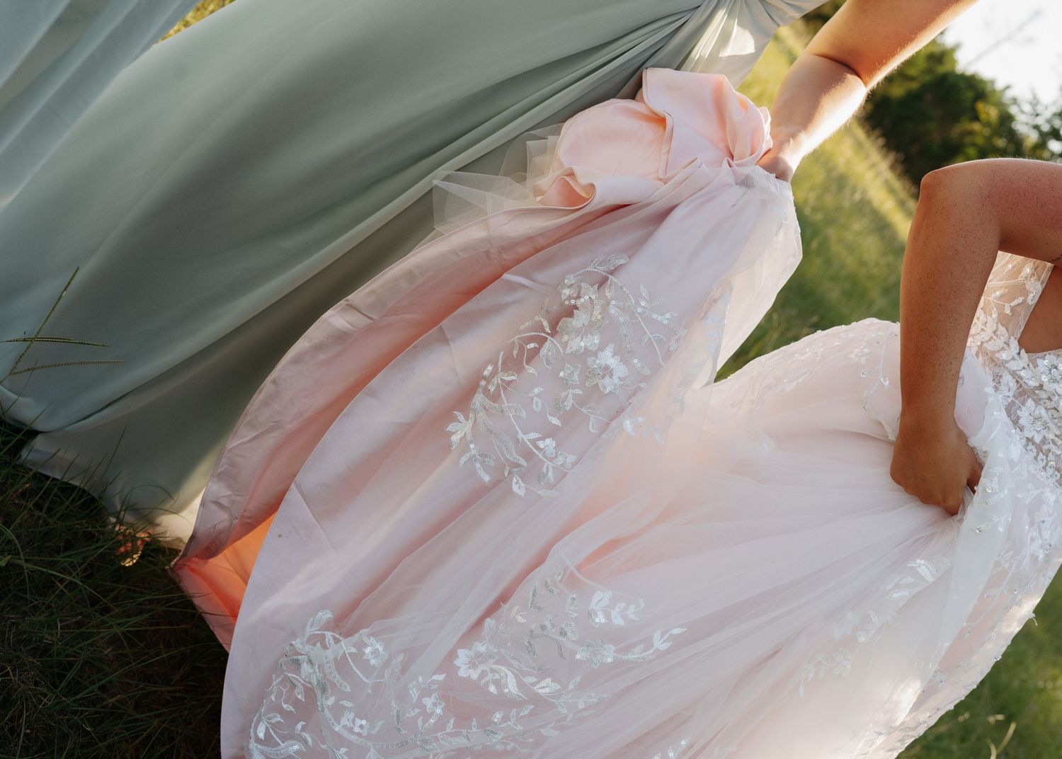 Close-up of a bride's blush pink and white lace ball gown wedding dress train outdoors.