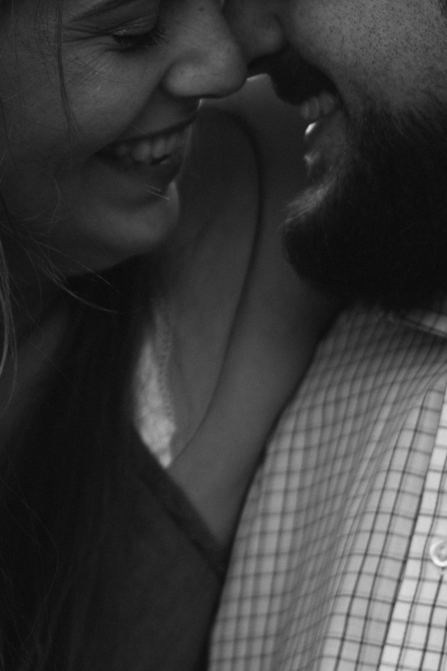 Black and white photo of a smiling couple sharing an intimate moment, the man nuzzling the woman's cheek tenderly.