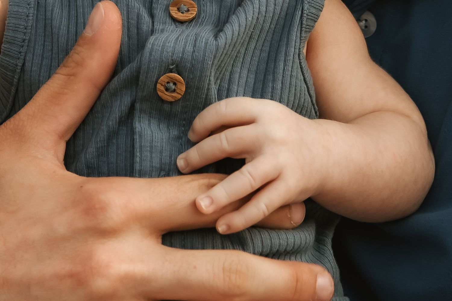 Close-up of small child's hand touching buttons on grey clothing.