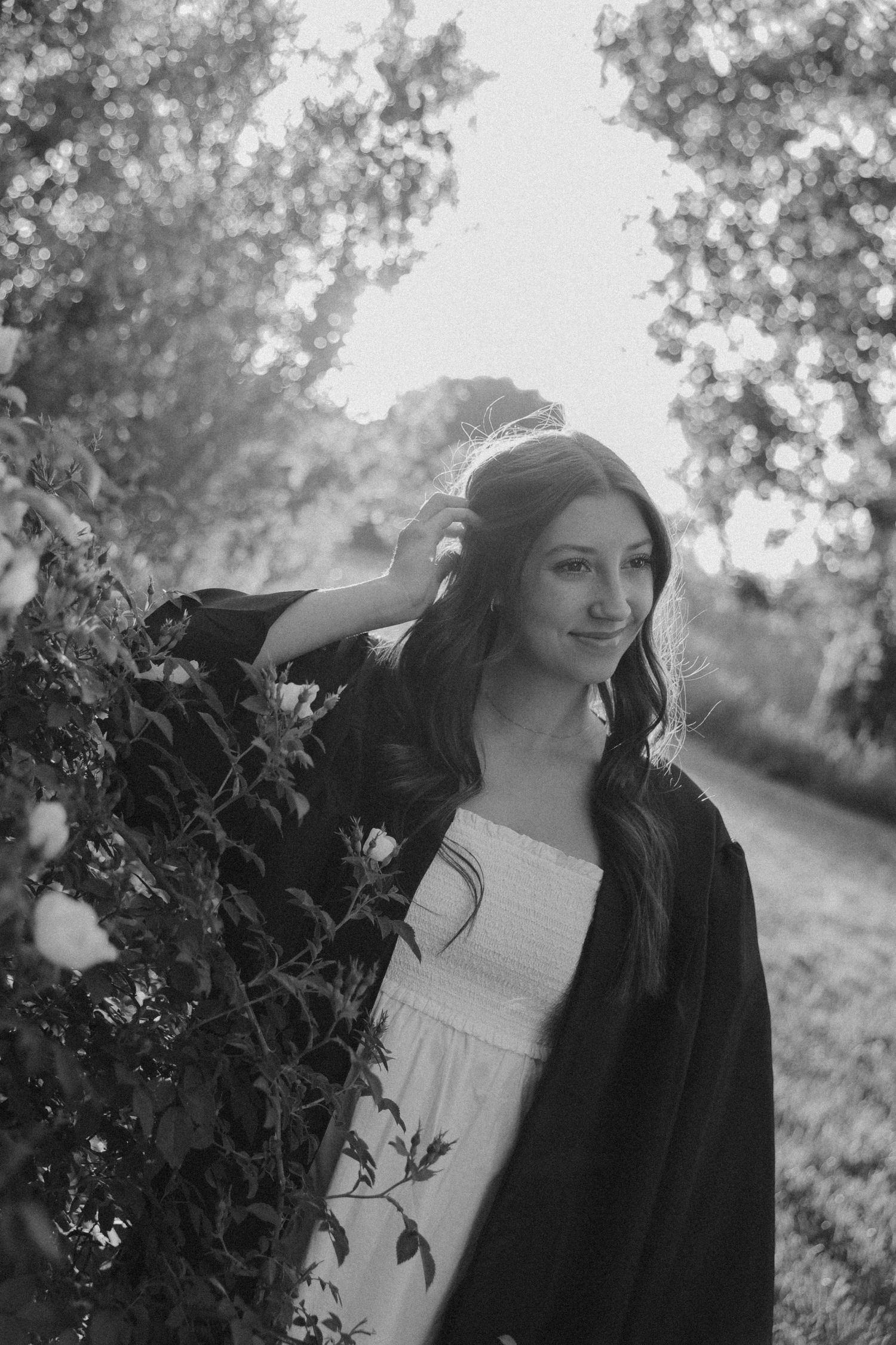 Black and white portrait in nature showing figure in dark clothing against soft foliage background.