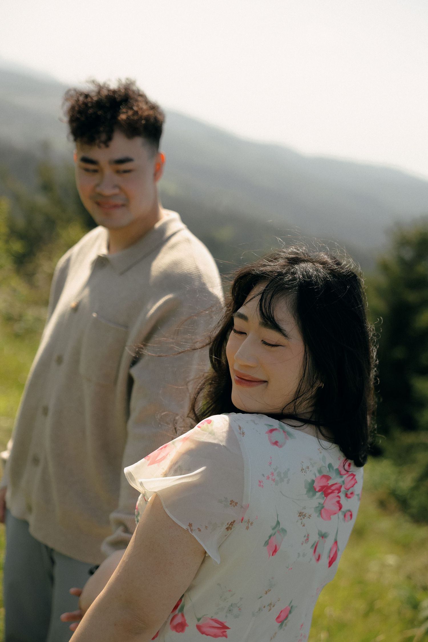 A couple enjoys a playful moment together on a sunny hillside.